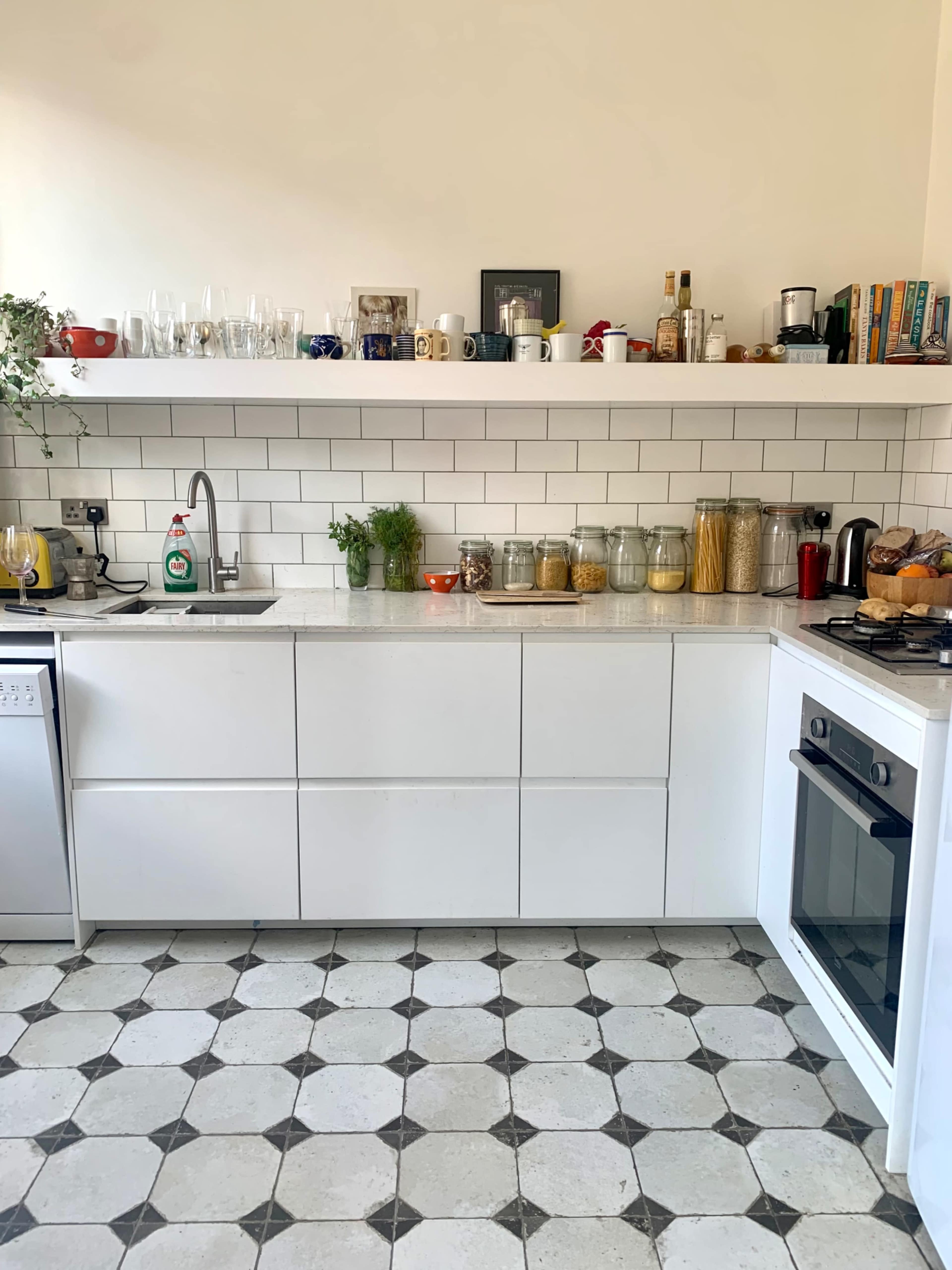A modern kitchen with white cabinetry, a tiled backsplash, and various jars and utensils arranged neatly on open shelves.