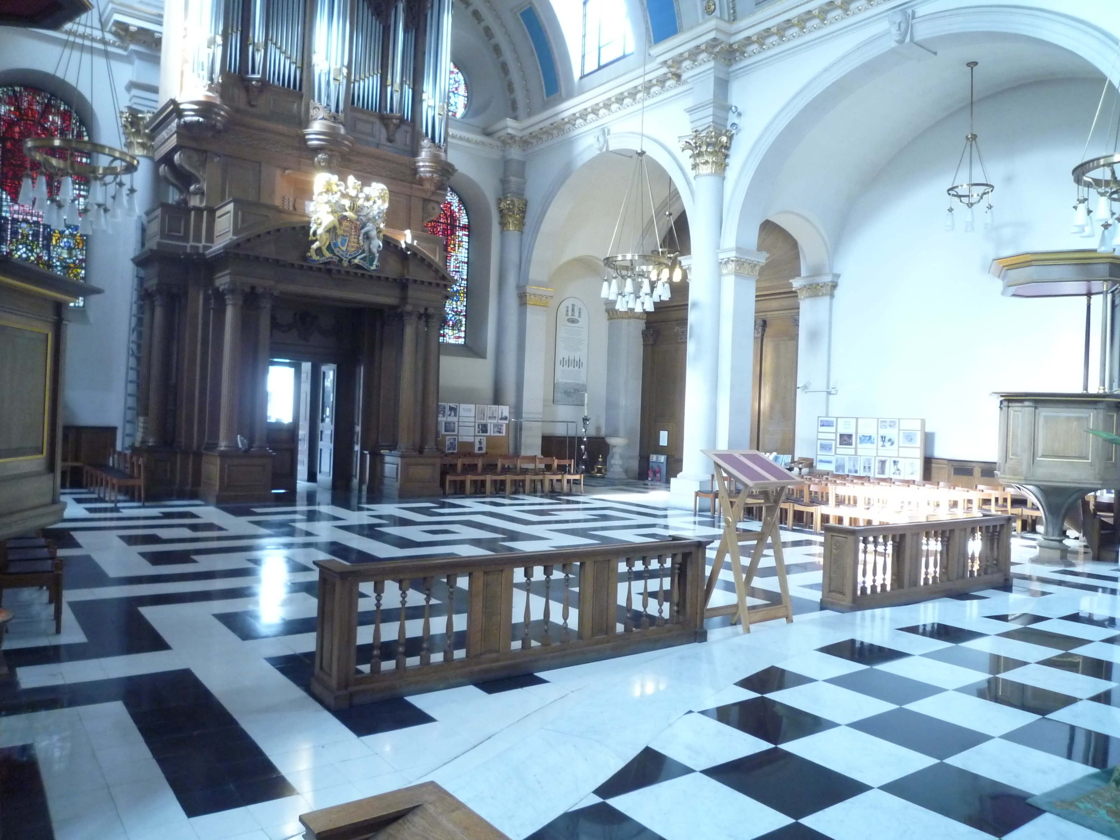 The interior of a large church features a checkerboard floor, wooden pews, and tall stained glass windows.