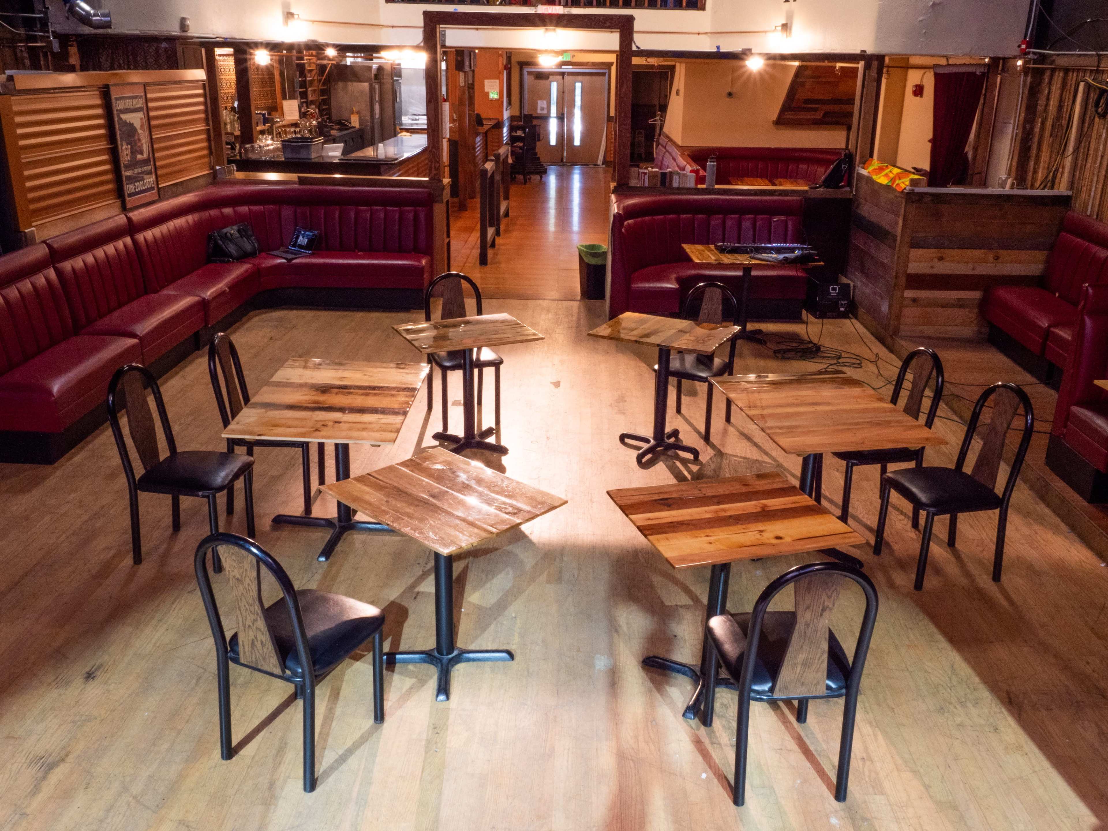 The image shows a spacious restaurant interior with multiple wooden tables and chairs arranged in the center, surrounded by red upholstered seating along the walls.
