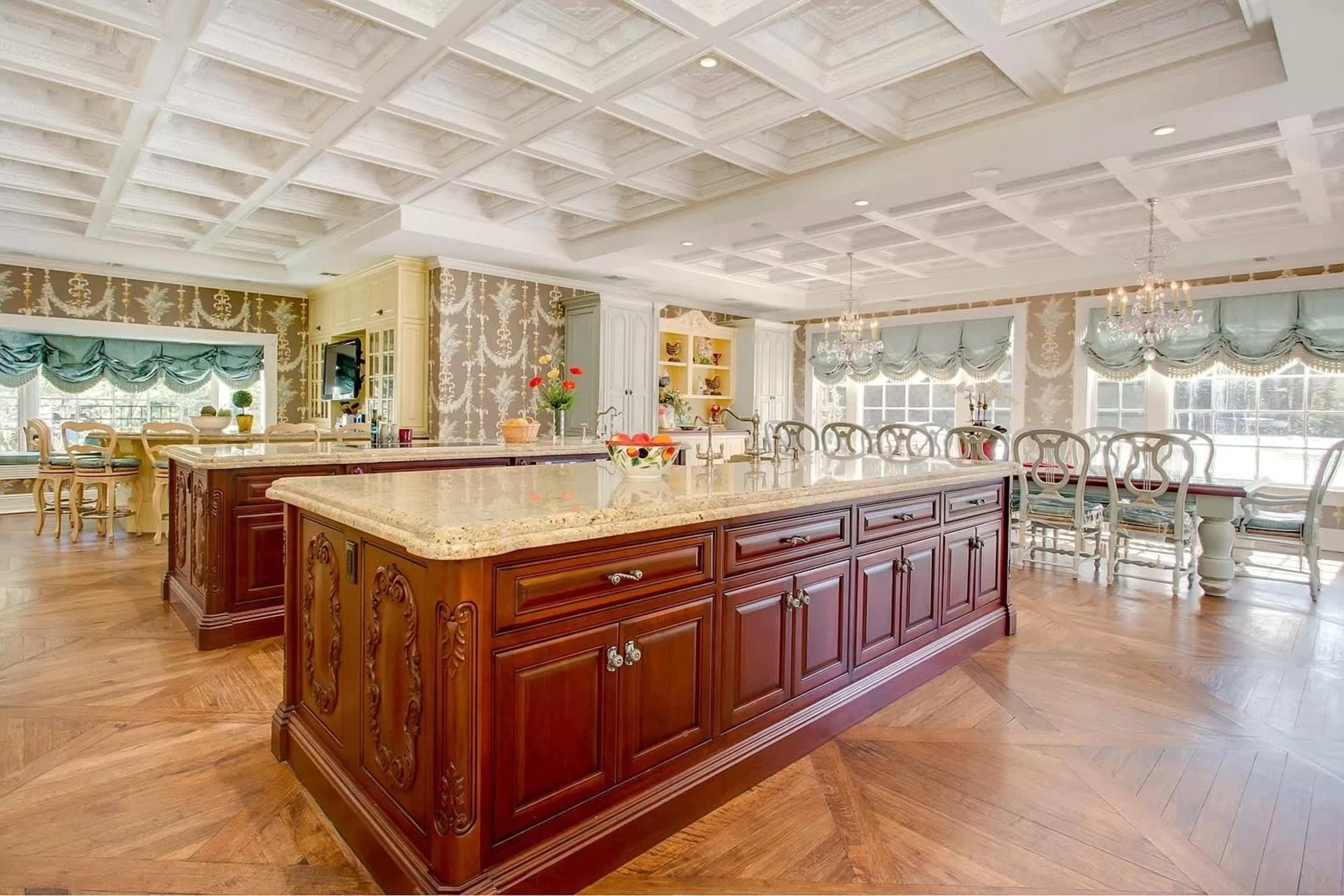 A spacious kitchen with a large wooden island, elegant cabinetry, and decorative ceiling tiles, surrounded by dining areas and large windows.