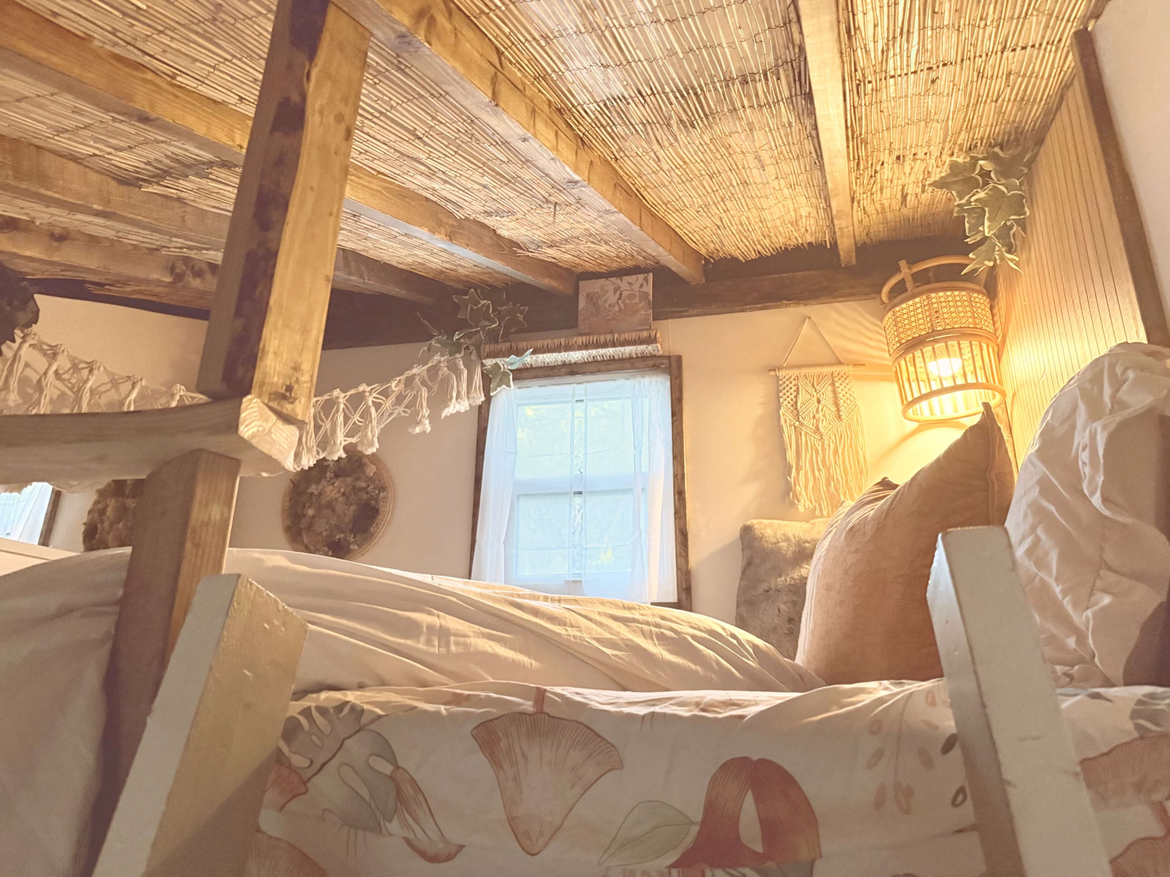 The image shows a cozy lofted bed in a rustic room with wooden beams, soft bedding, and warm lighting.
