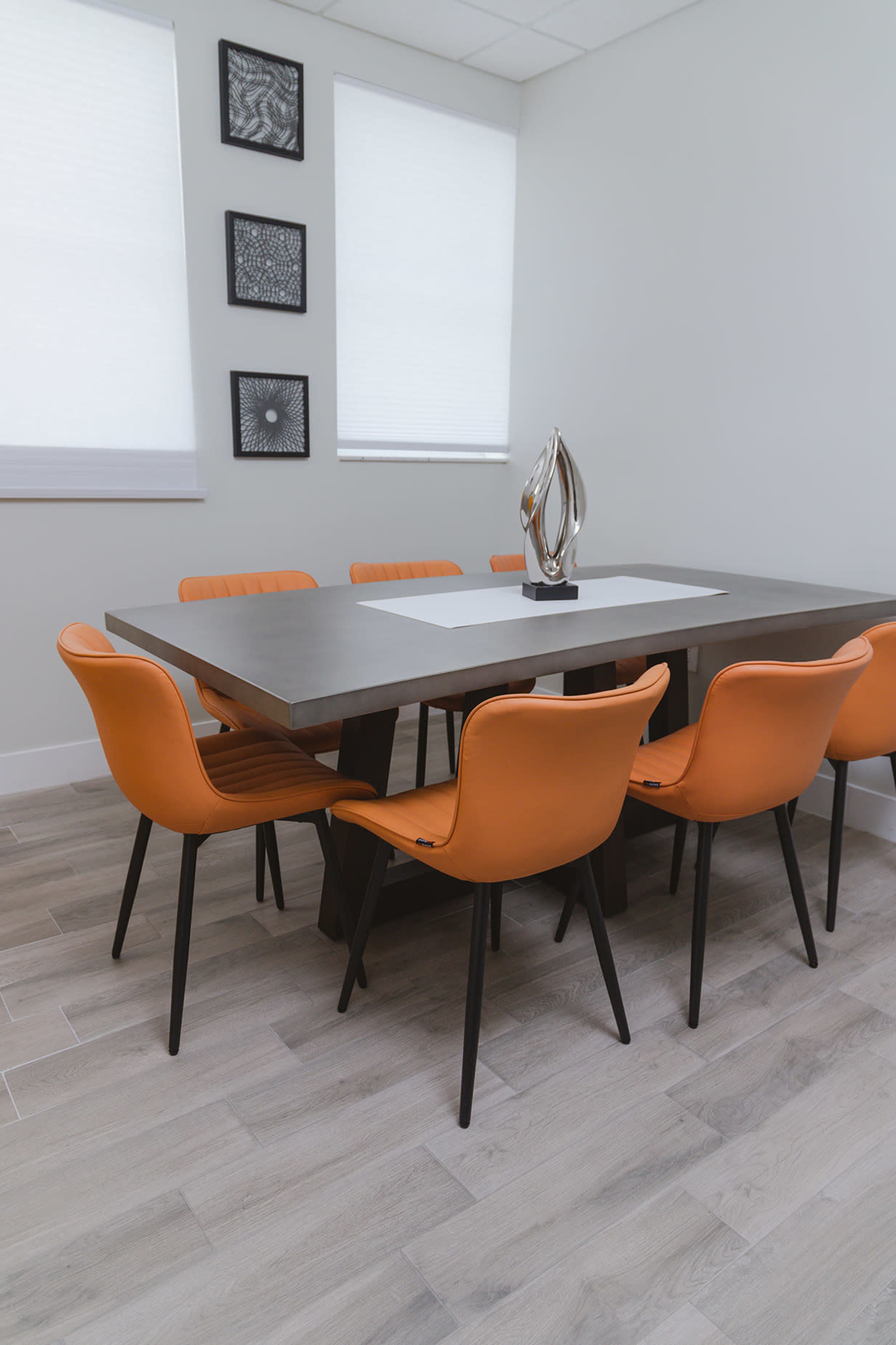 A modern dining room features a rectangular table surrounded by six orange chairs, with abstract artwork on the walls.