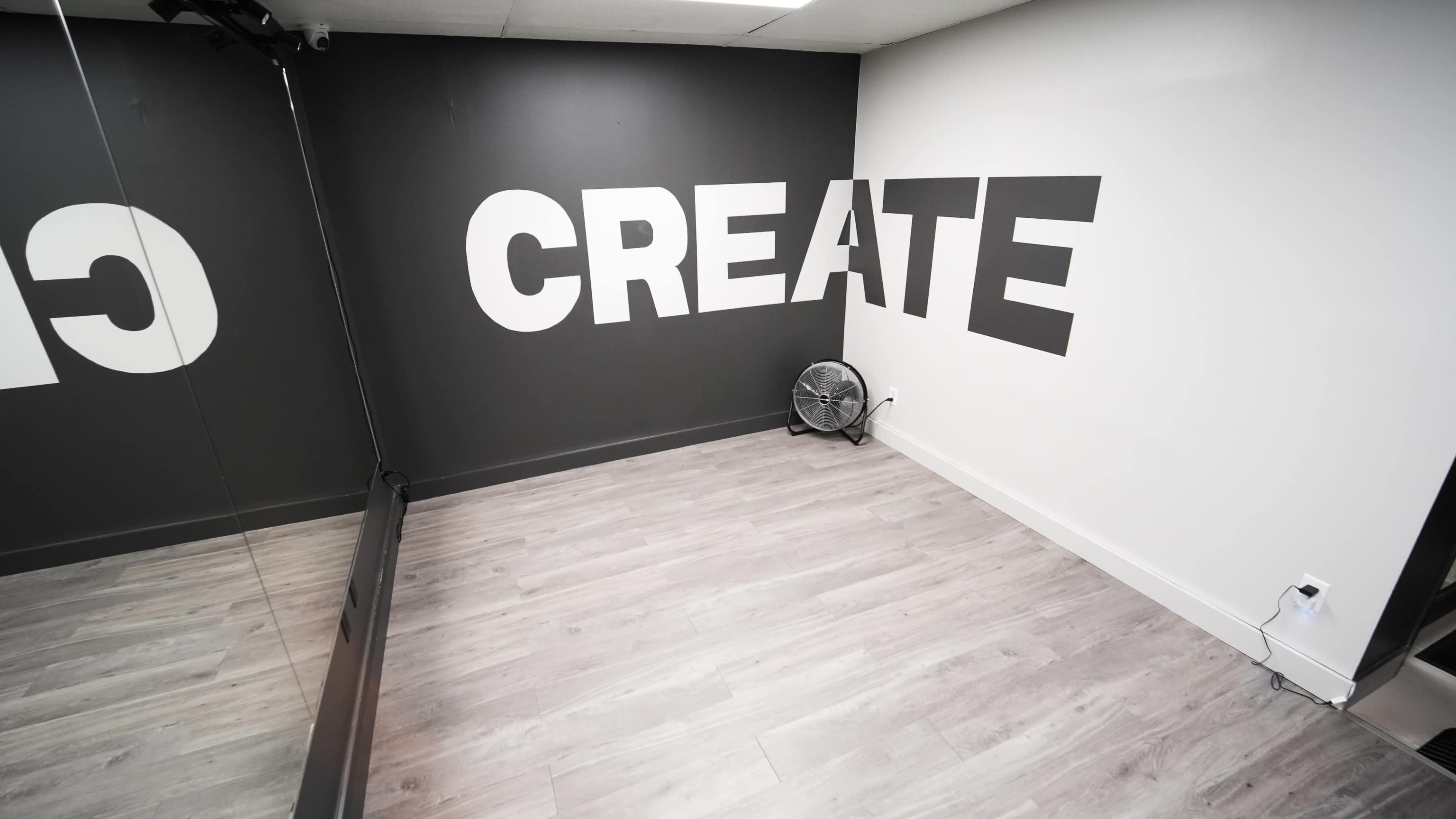 The room features a large wall painted with the word "CREATE" in bold letters, a mirror along one side, and a small fan on the floor.