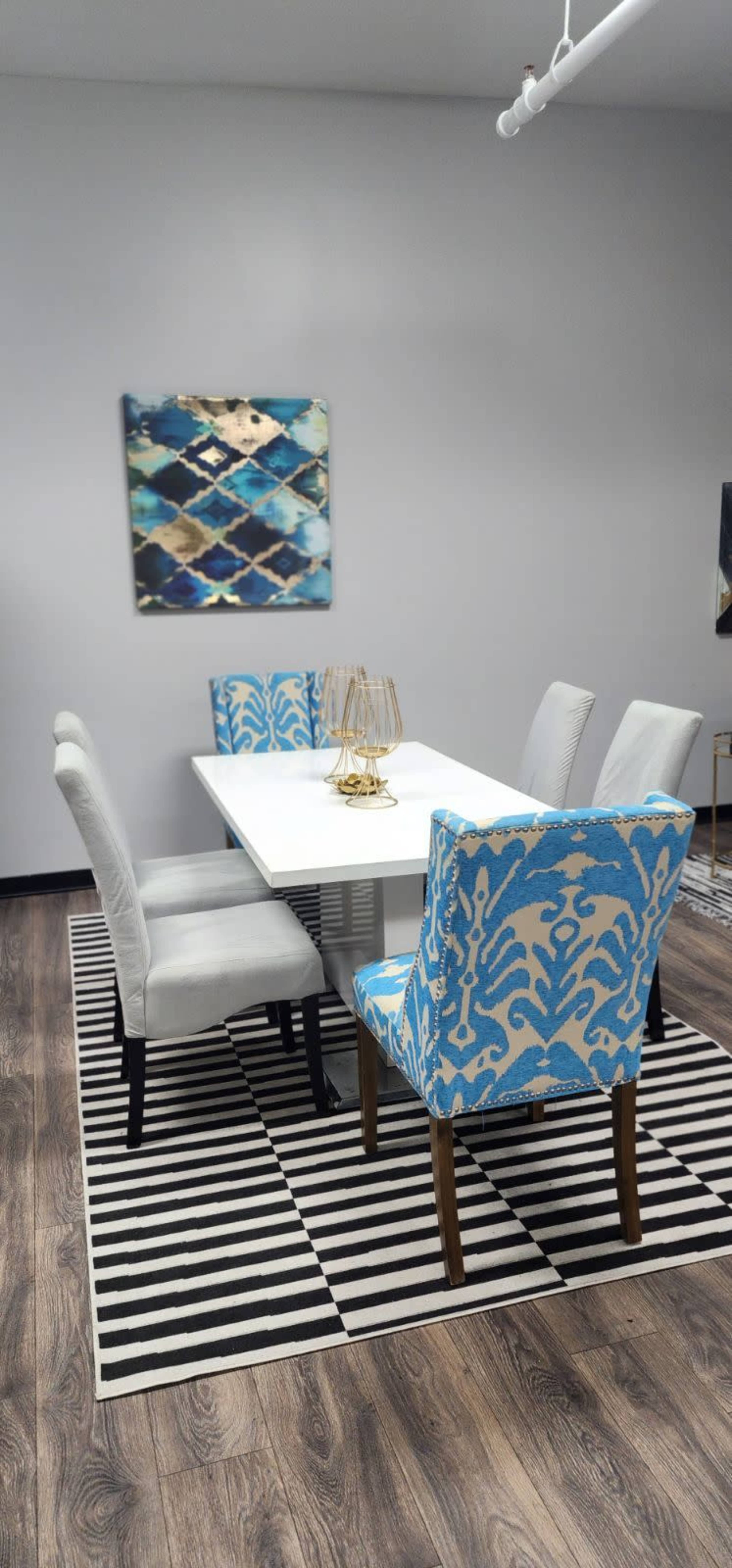 A modern dining room features a white table surrounded by four patterned chairs and a striped rug.