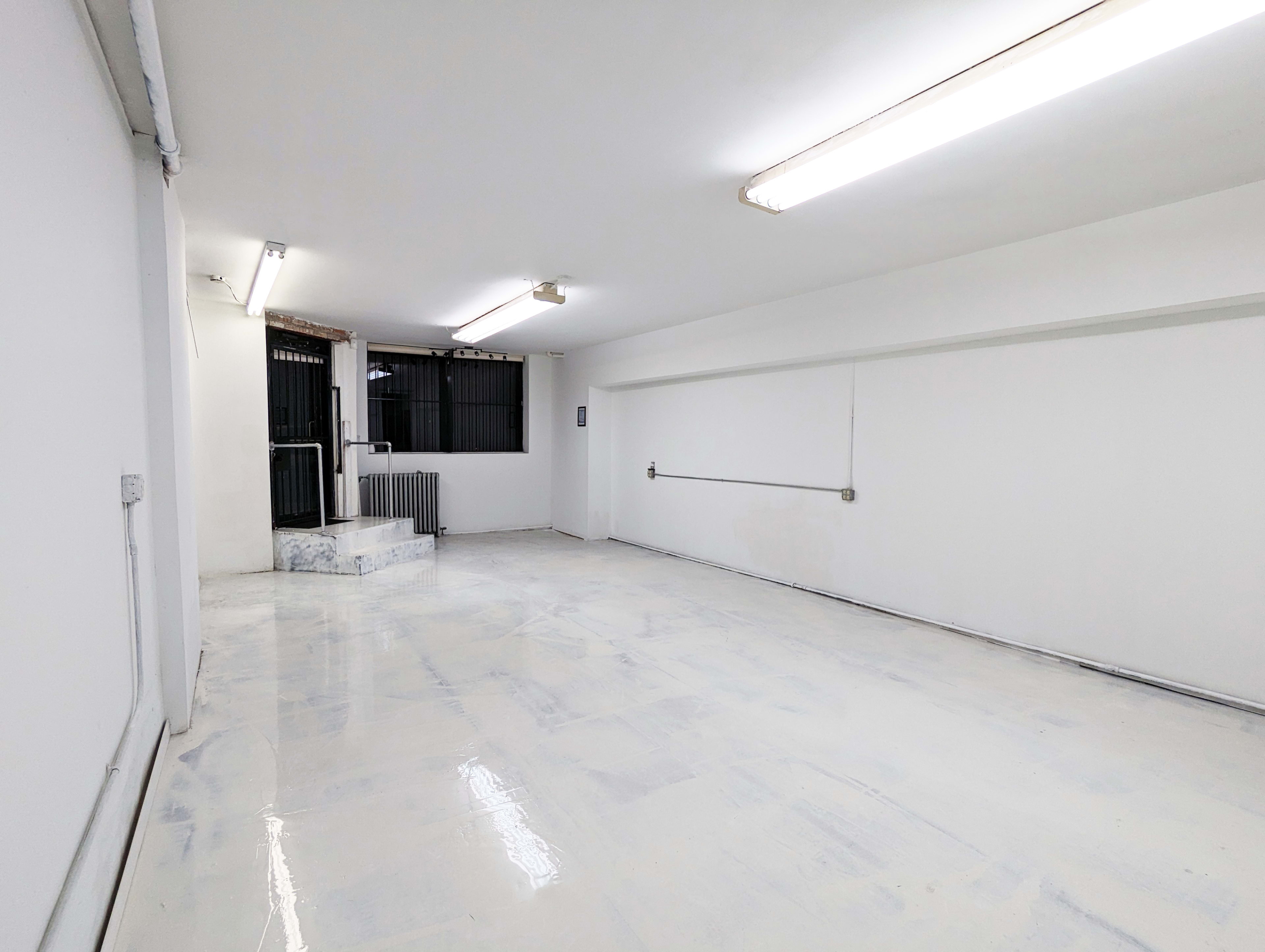 The image shows a vacant room with white walls and a glossy floor, featuring a small set of steps leading to a window.