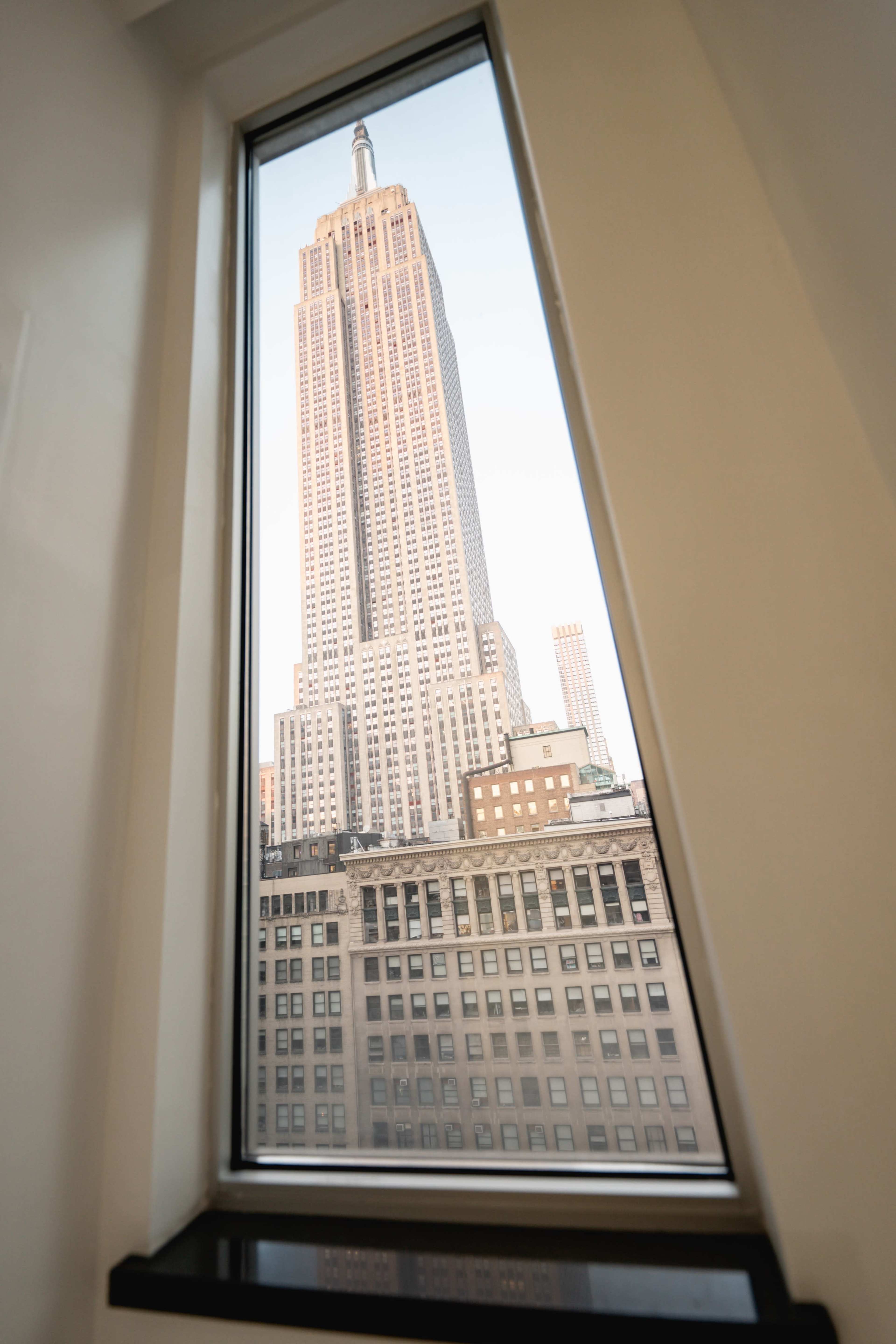 The Empire State Building rises prominently outside a large triangular window.