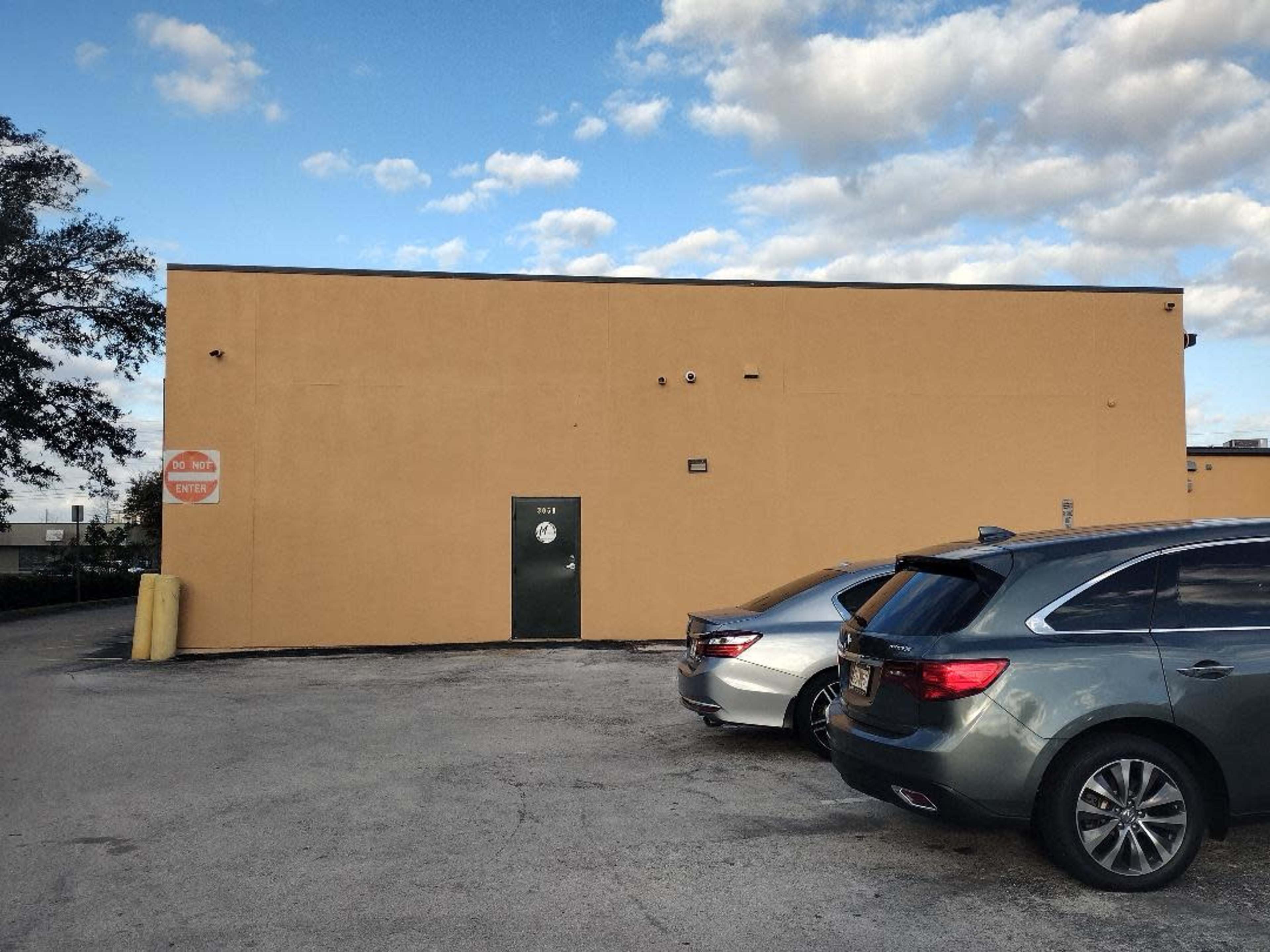 A yellow building with a green door and two parked cars is shown under a partly cloudy sky.