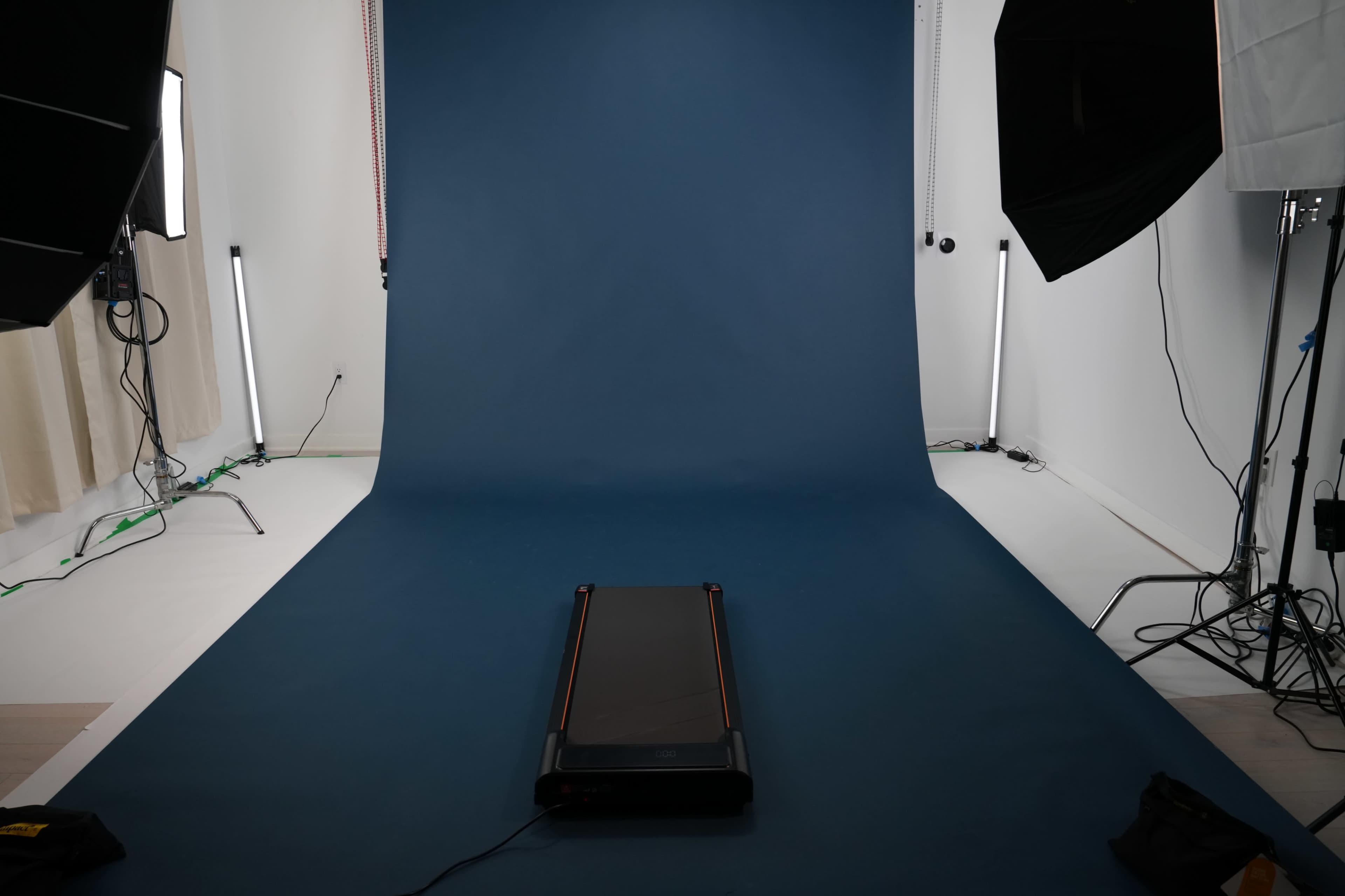 The image shows a treadmill placed on a blue backdrop in a photography studio with lights positioned around the area.