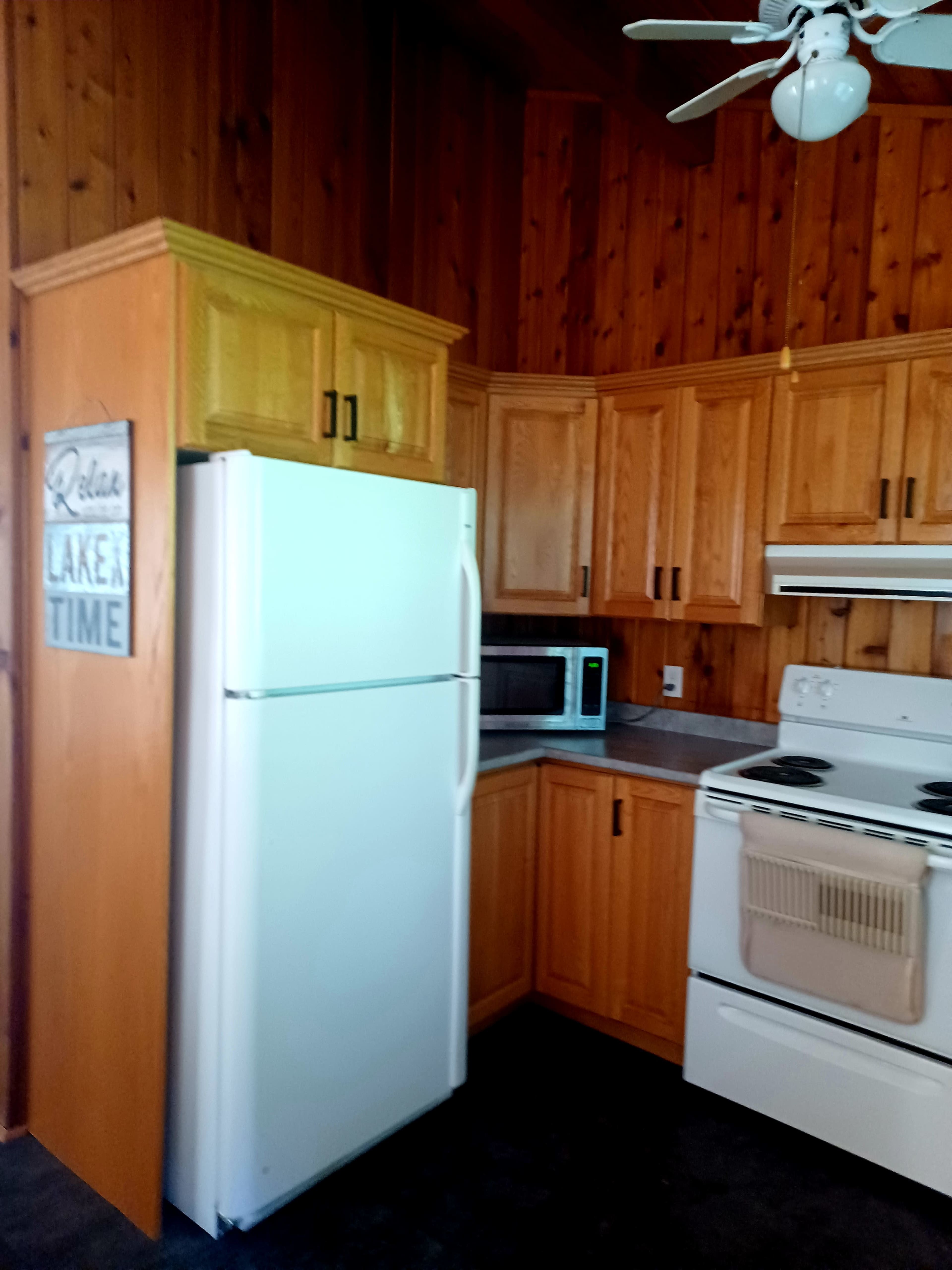 A kitchen with wooden cabinetry, a white refrigerator, a microwave, and a stove against a paneled wall.