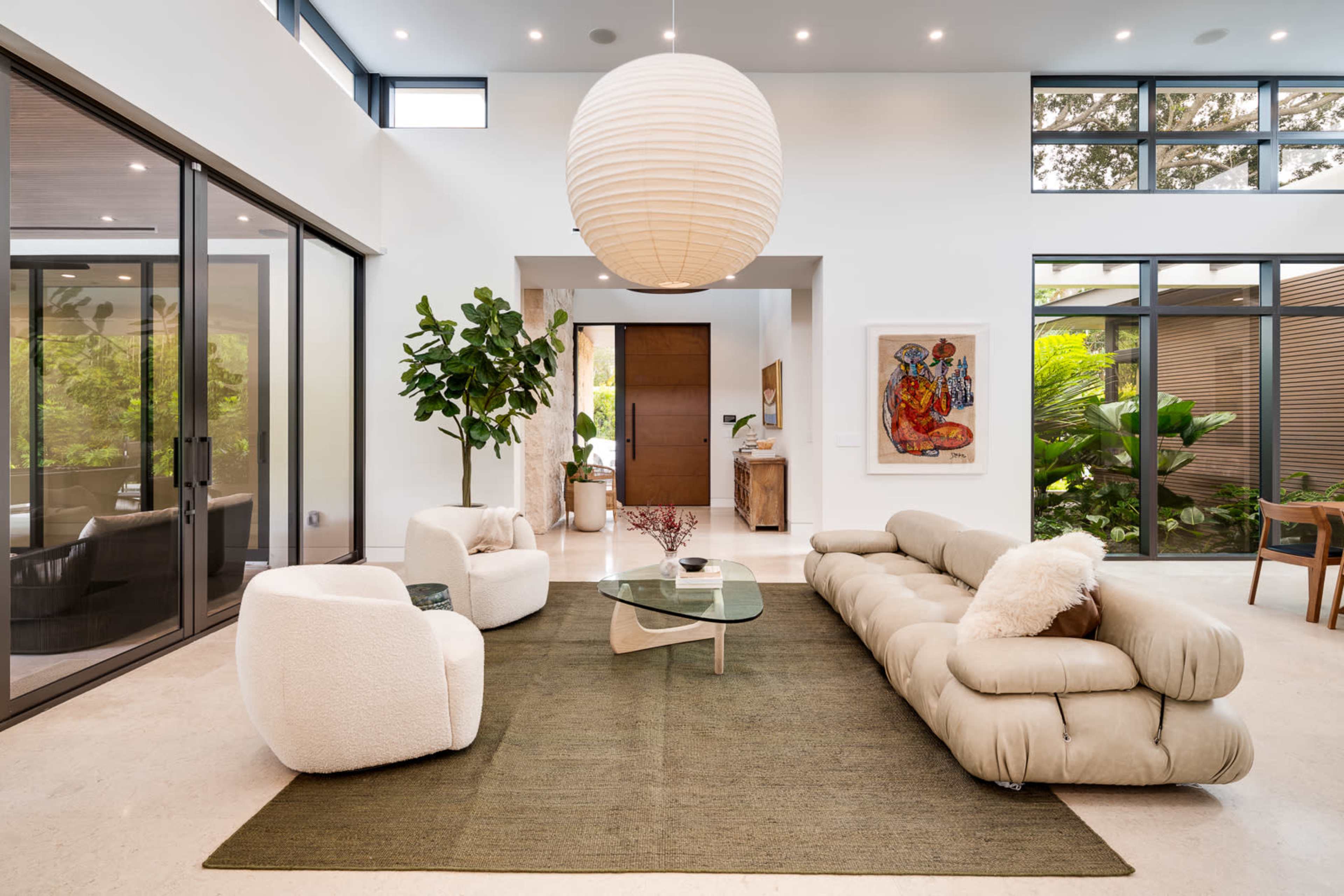 The living room features a contemporary sofa, two plush armchairs, a glass coffee table, and large windows allowing natural light to illuminate the space.