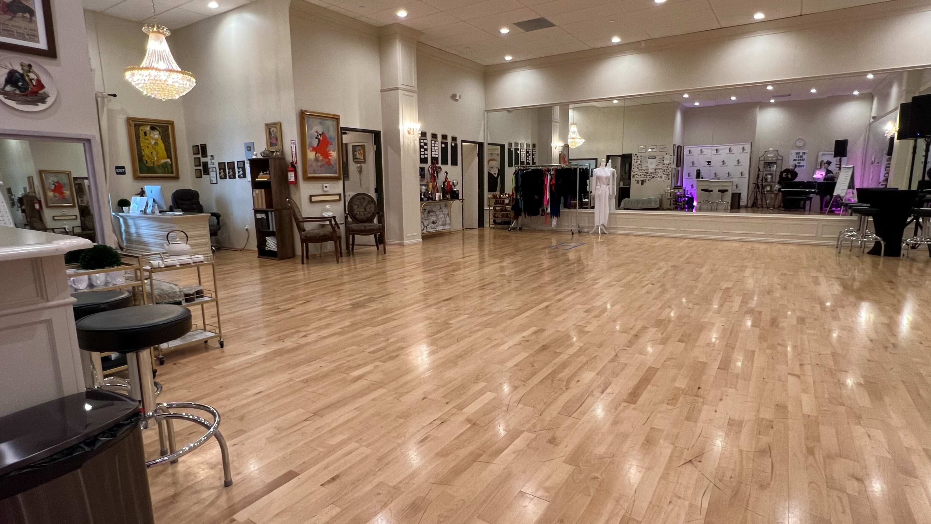 A spacious dance studio with wooden flooring, mirrors, and various clothing racks along the walls.