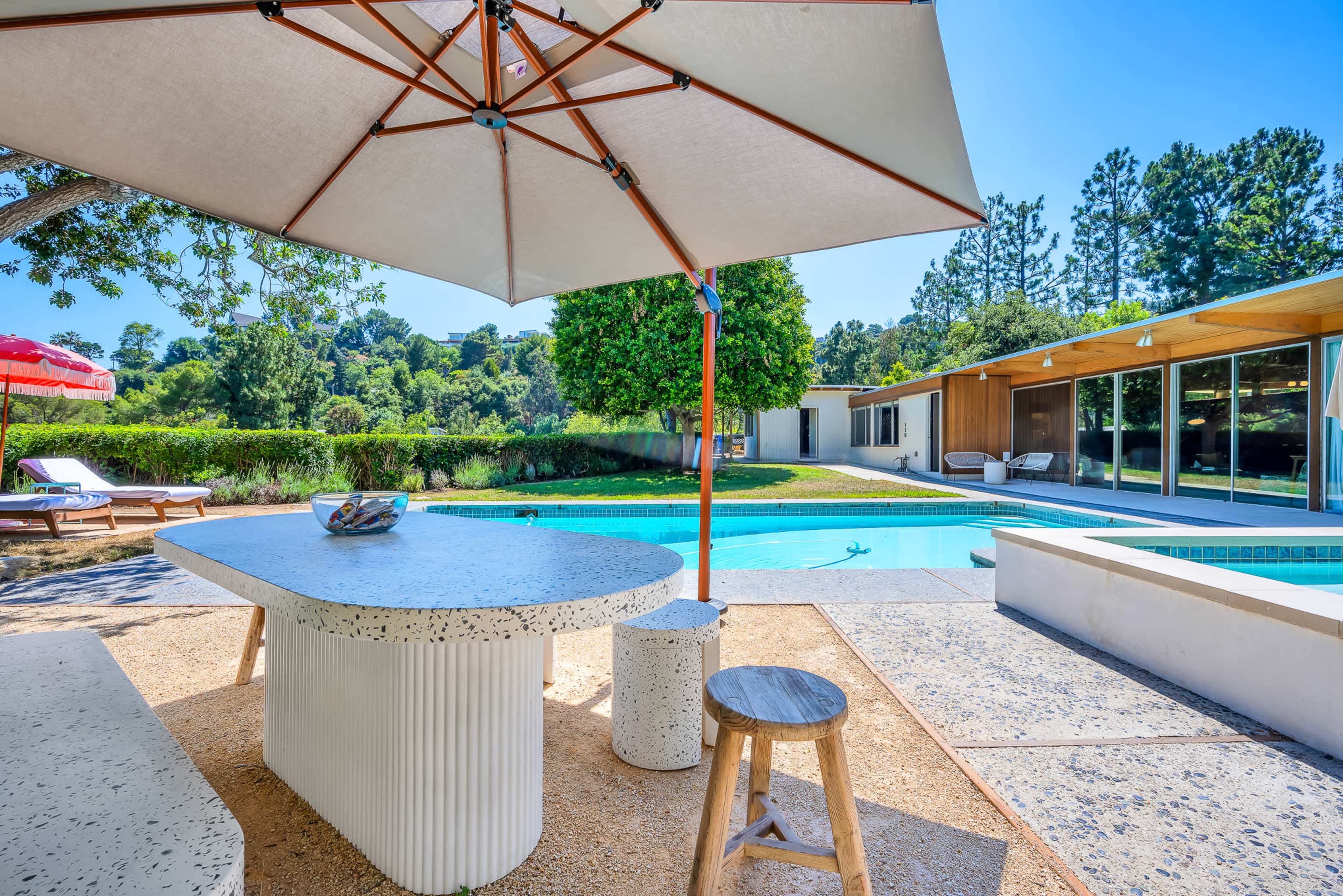 A modern outdoor space features a swimming pool surrounded by seating areas and shaded by a large umbrella.