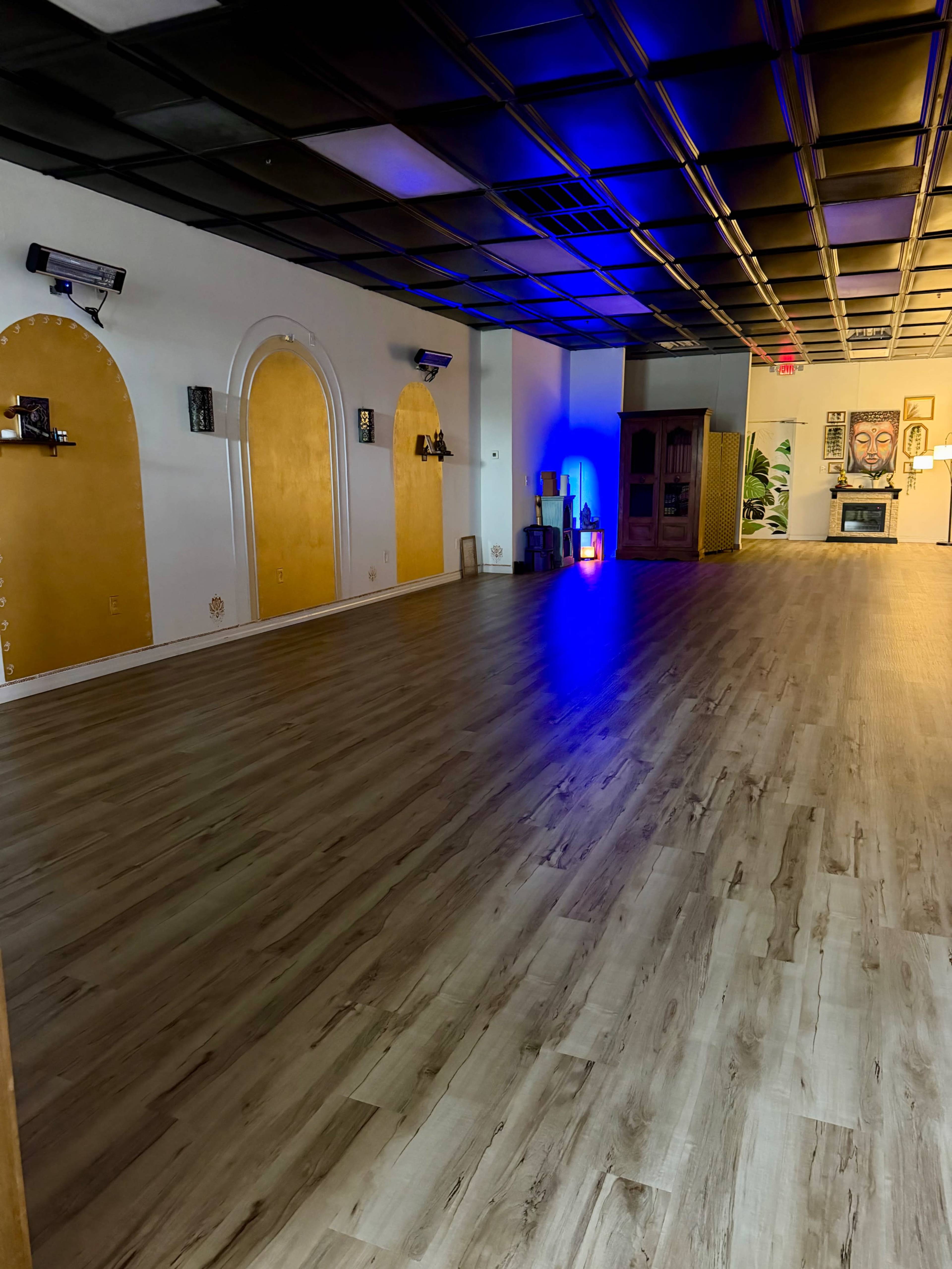 The image shows an empty room with wooden flooring, yellow archways on the walls, and colored lights in one corner.