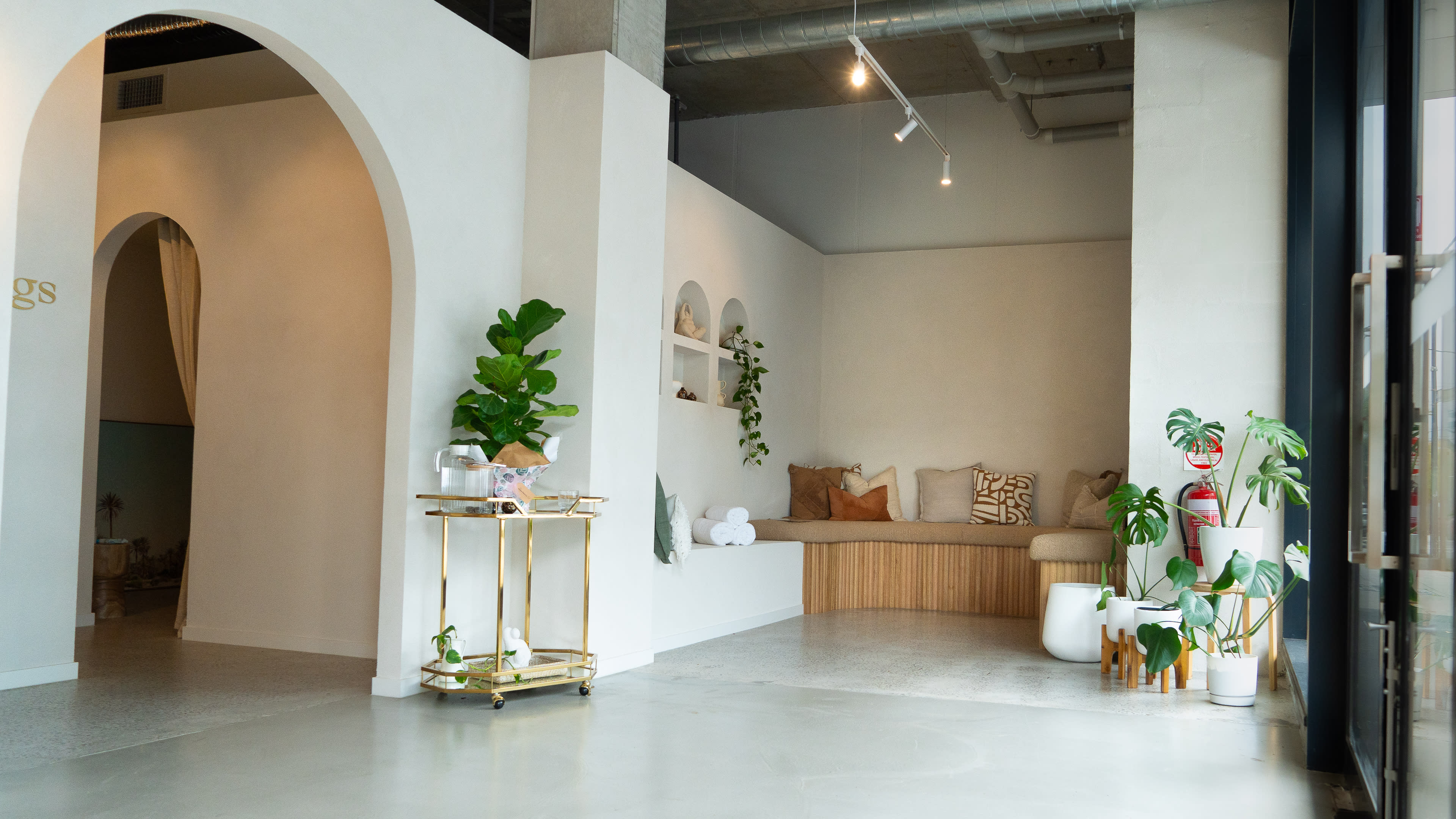 The image shows a modern interior space featuring a seating area with a wooden bench, decorative plants, and minimalist decor.