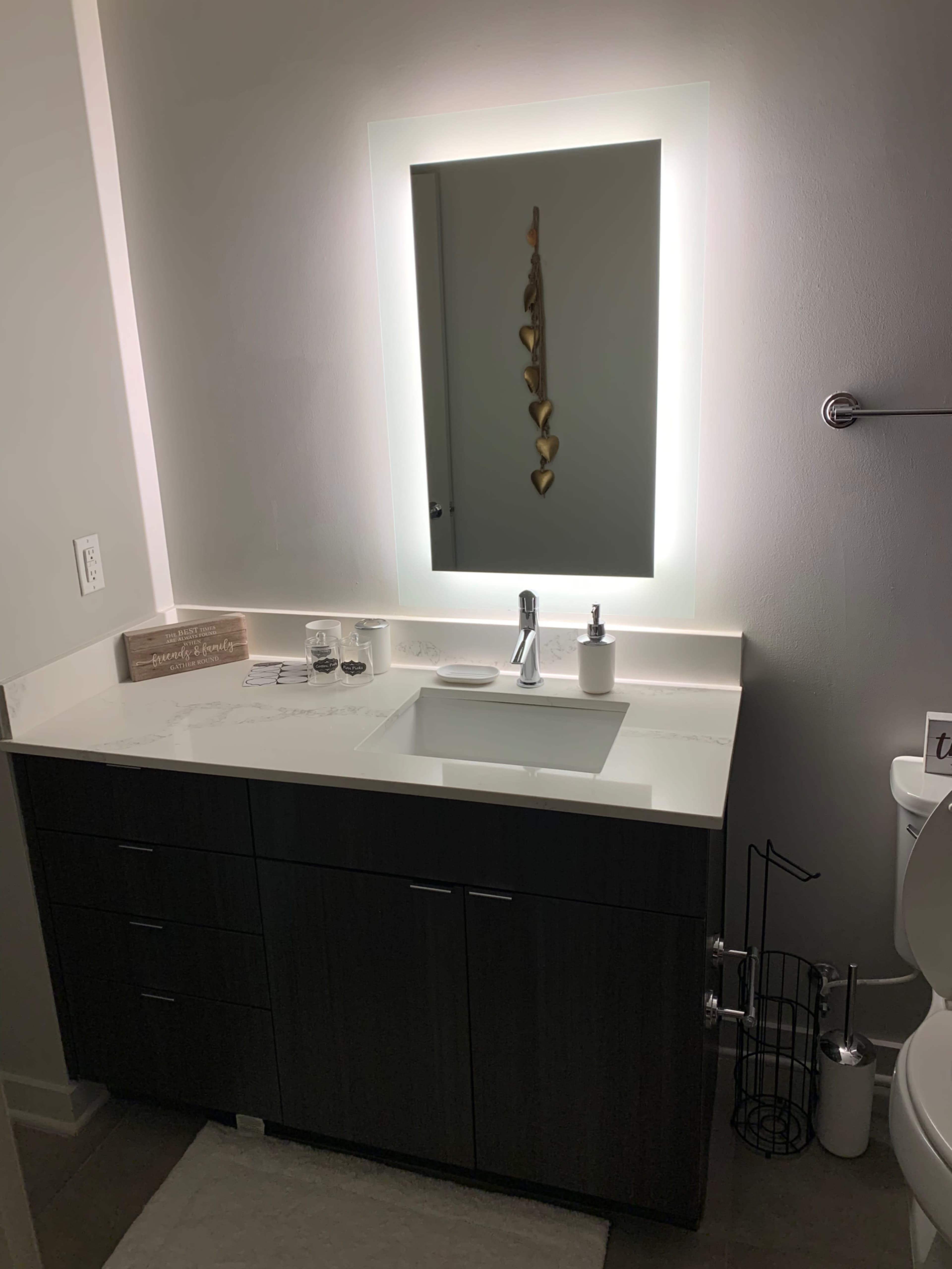 A modern bathroom vanity with a sink, faucet, illuminated mirror, and dark cabinetry.