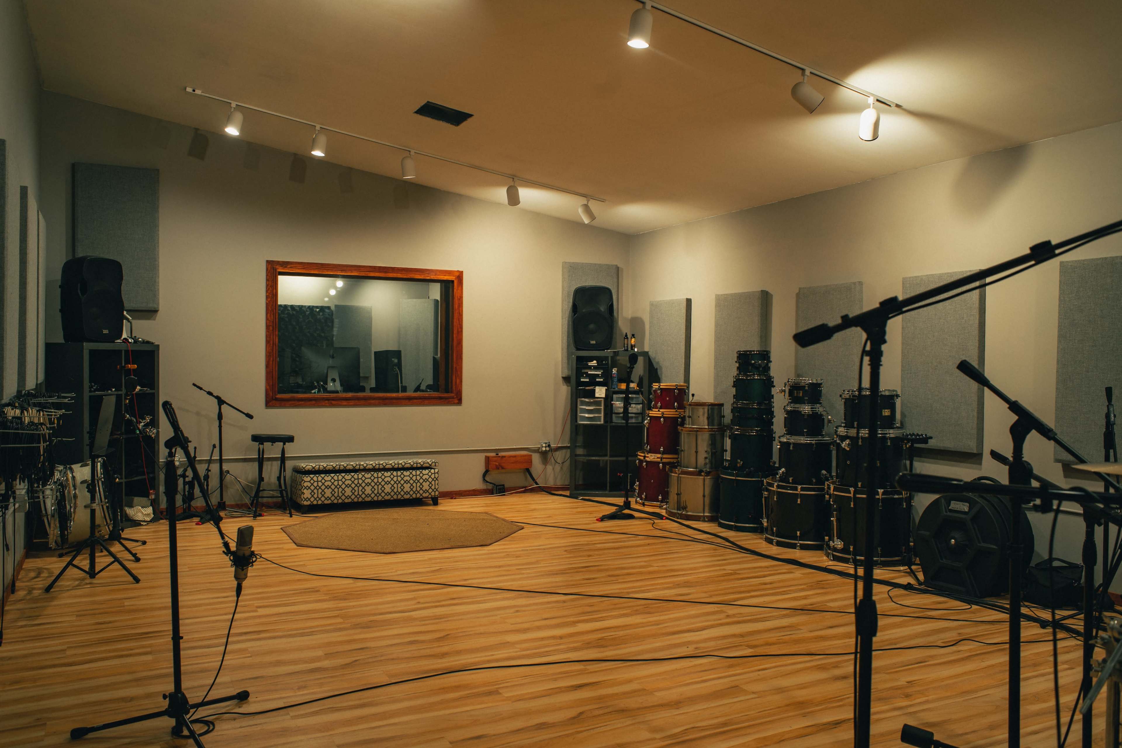 A spacious recording studio featuring various musical instruments, including guitars and a large collection of drums, along with soundproofing panels on the walls.