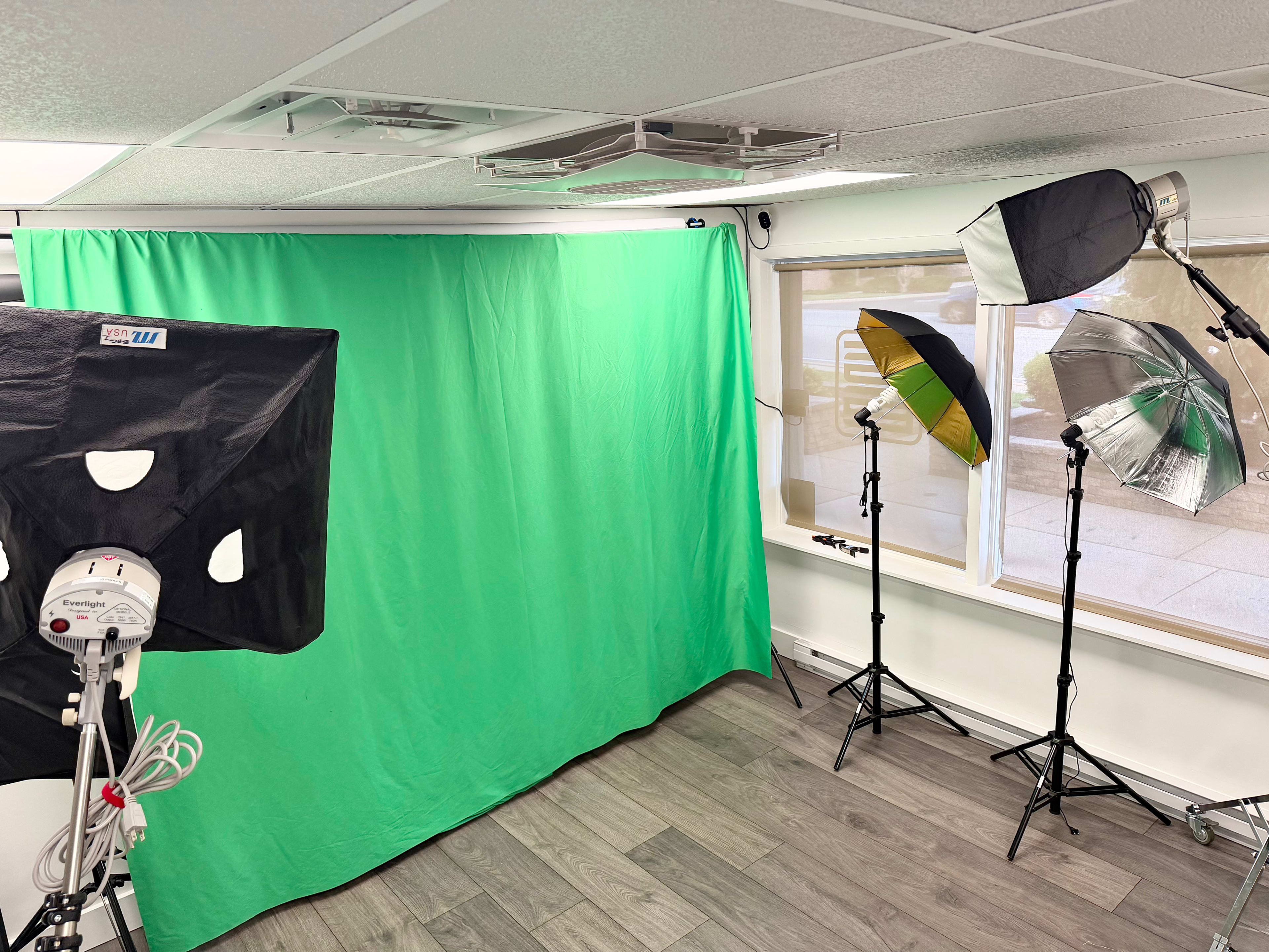 The image shows a photography setup featuring a green backdrop, three lighting umbrellas, and a floor surface in a well-lit room.