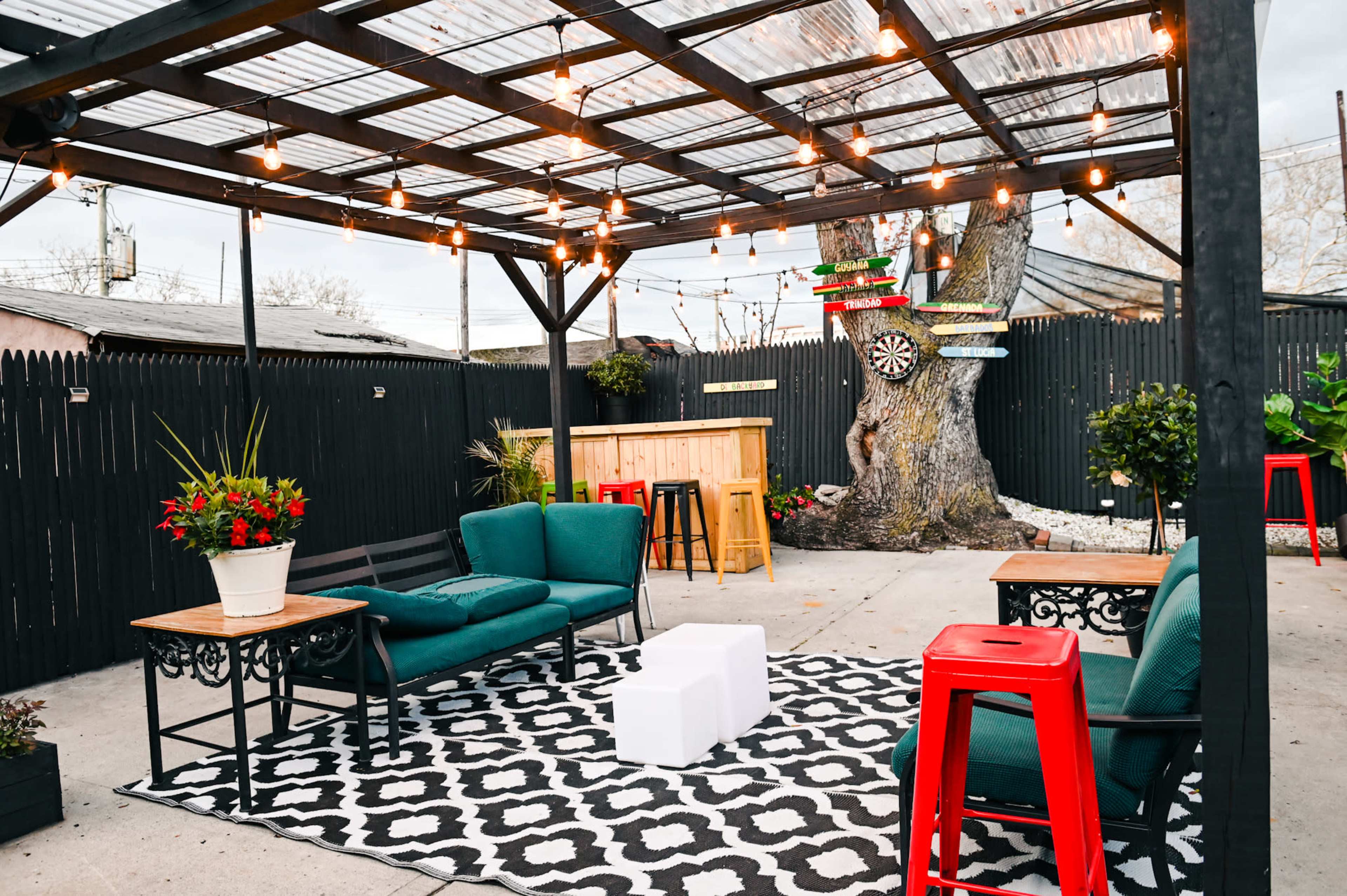 A cozy outdoor patio area with a black and white patterned rug, two green couches, red bar stools, and string lights overhead.