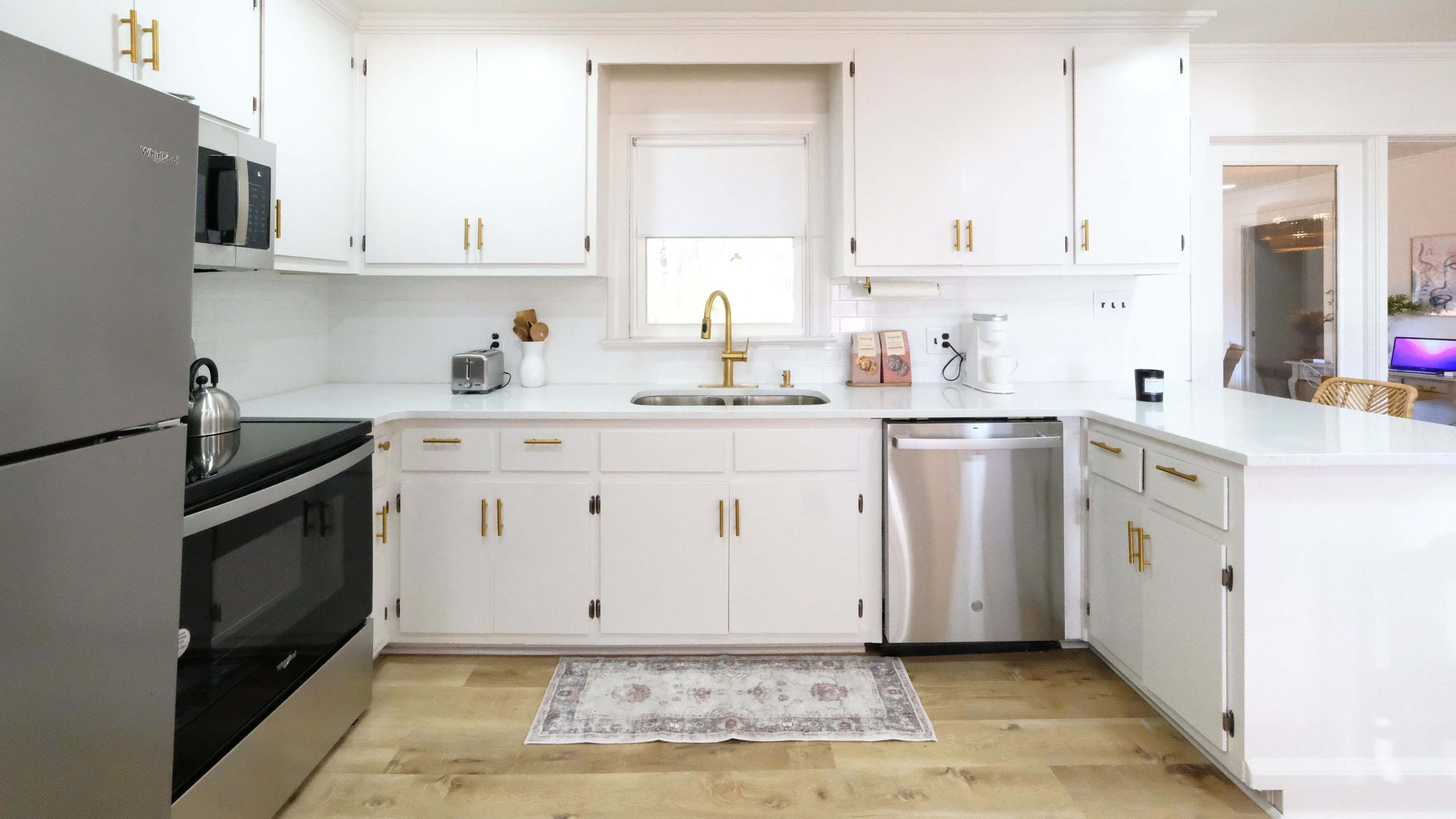 A modern kitchen with white cabinets, stainless steel appliances, and a central sink under a window.