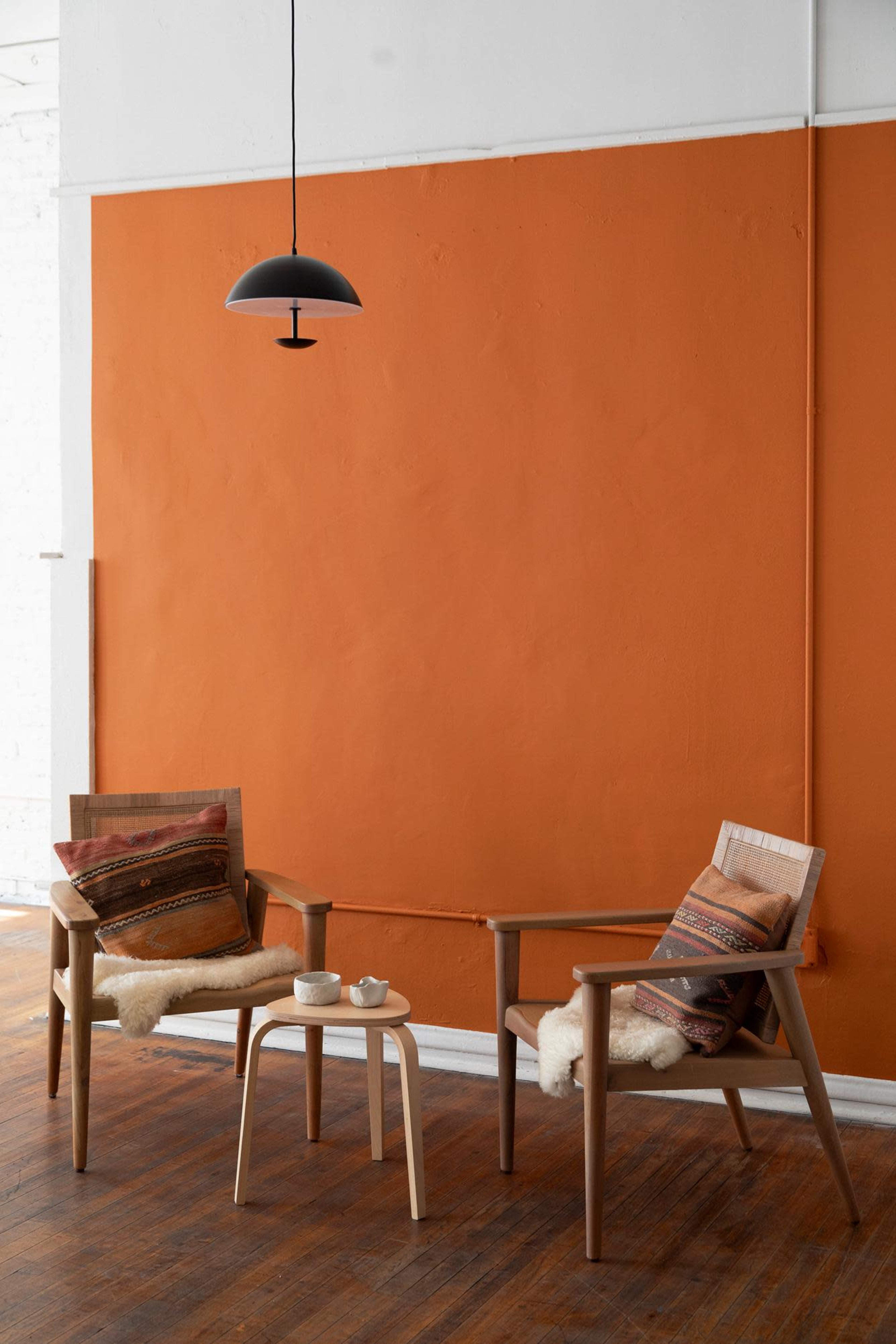 Two wooden chairs with patterned cushions and a small table set against an orange wall in a brightly lit room.