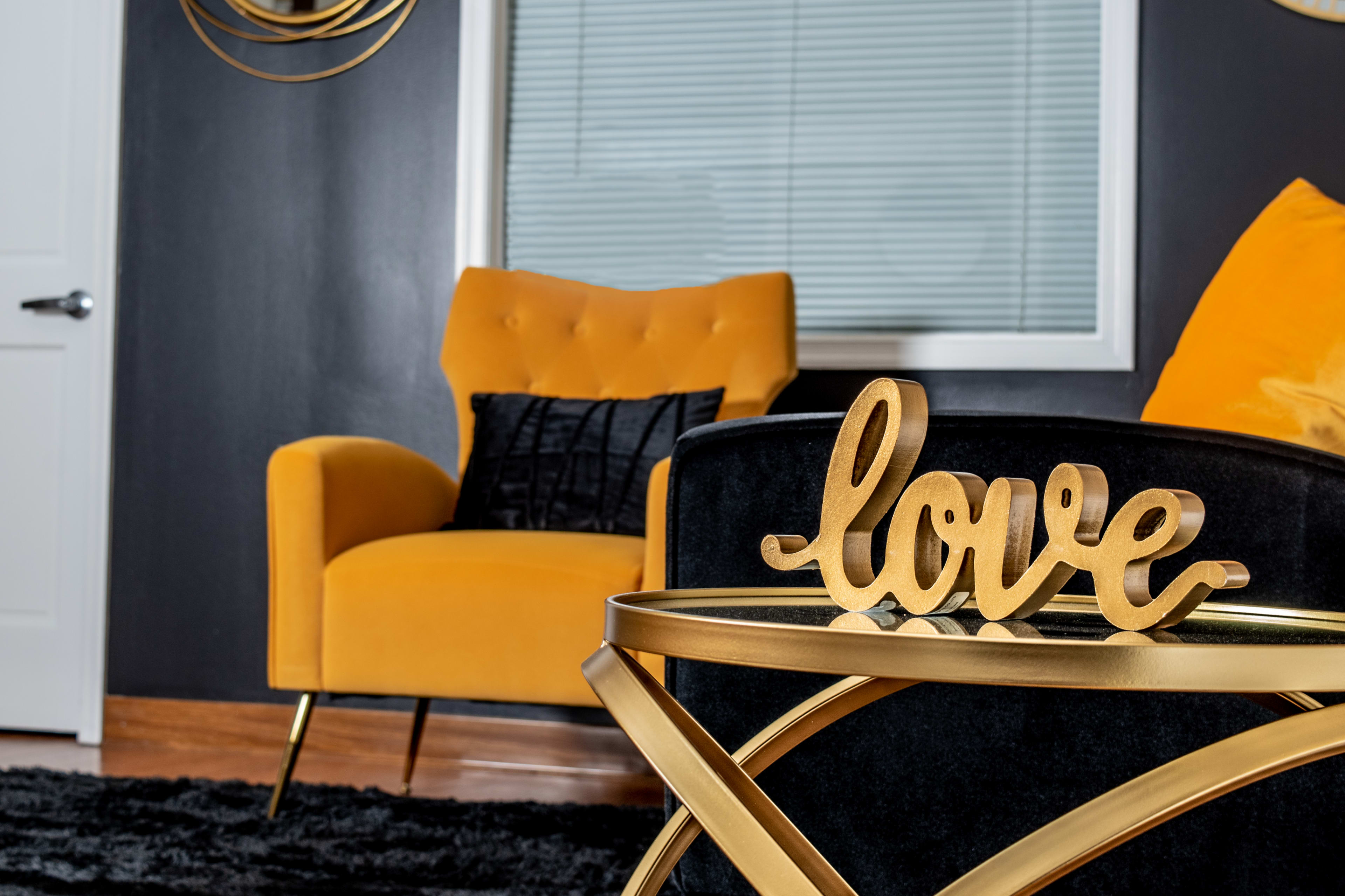 A wooden "love" sign rests on a gold-accented table in a room featuring a yellow armchair and black decor.