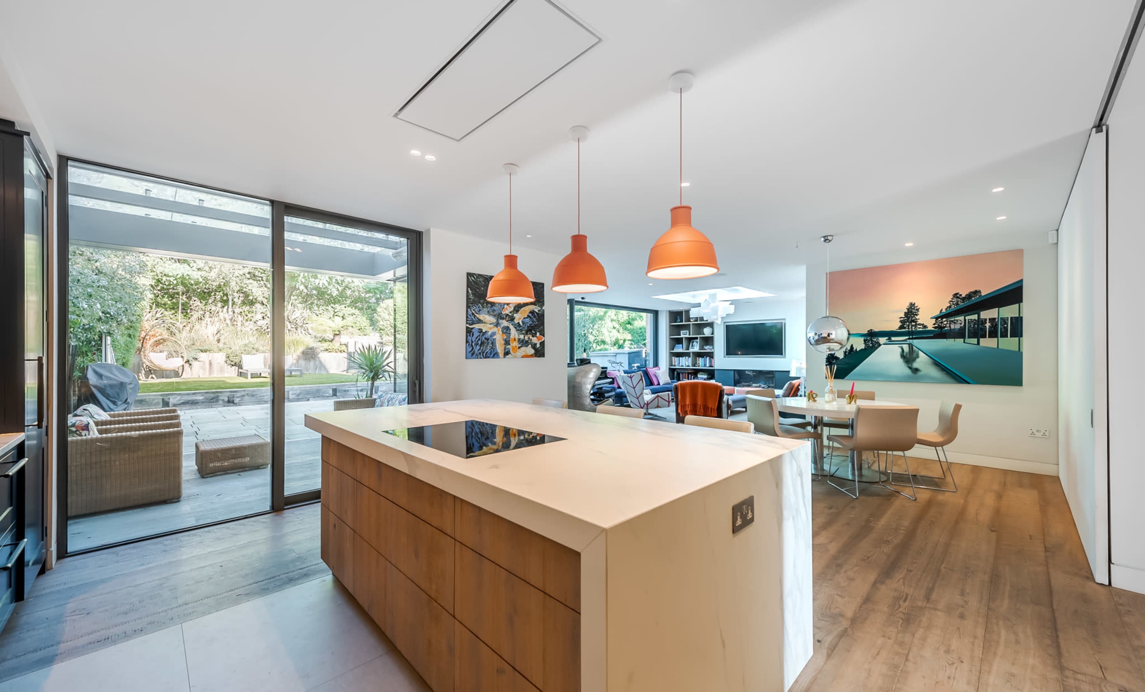 The image shows a modern kitchen with an island, pendant lights, and a view of an outdoor area through large glass doors.