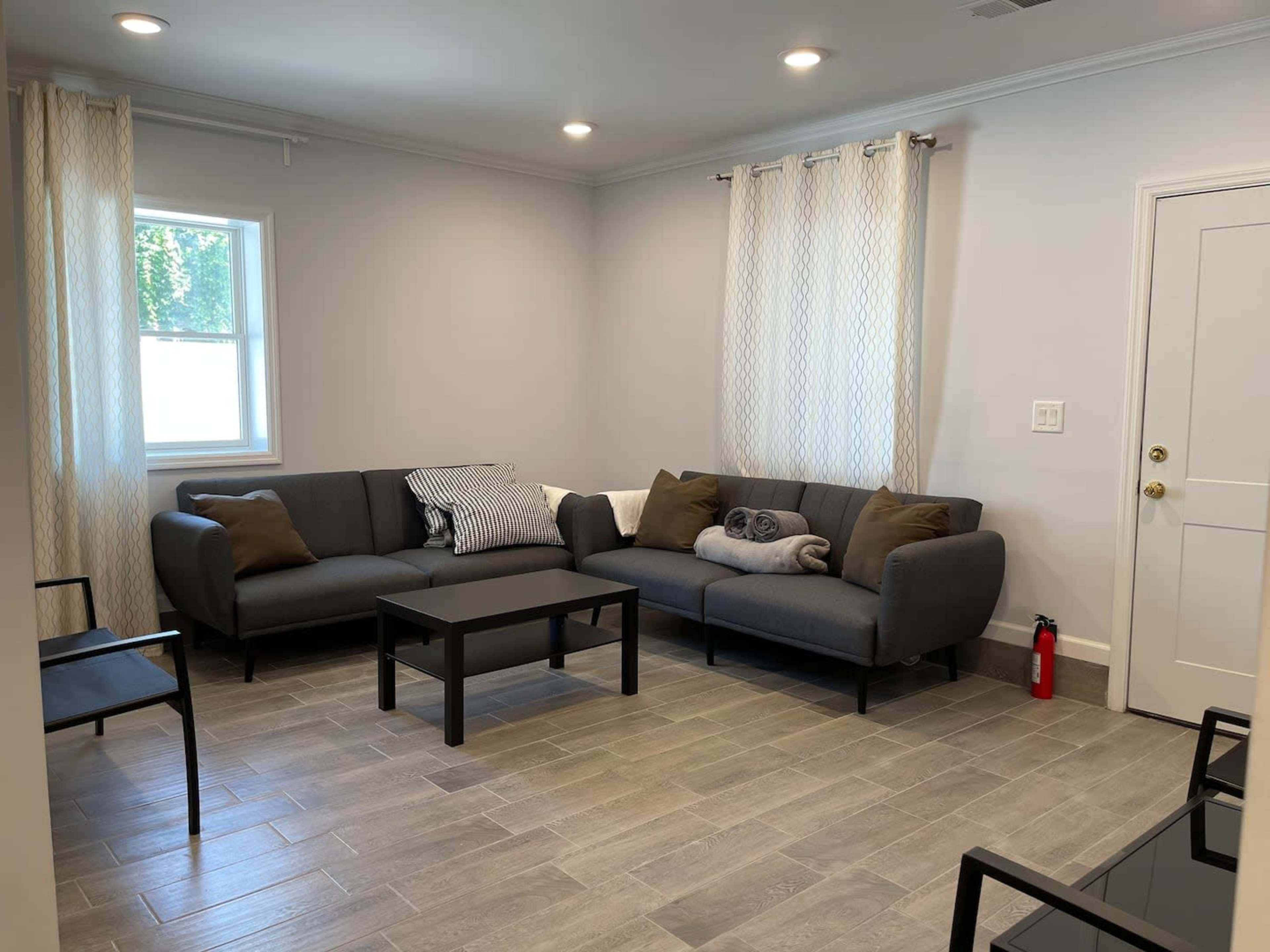 A modern living room with a sectional sofa, a coffee table, and two windows with light curtains.