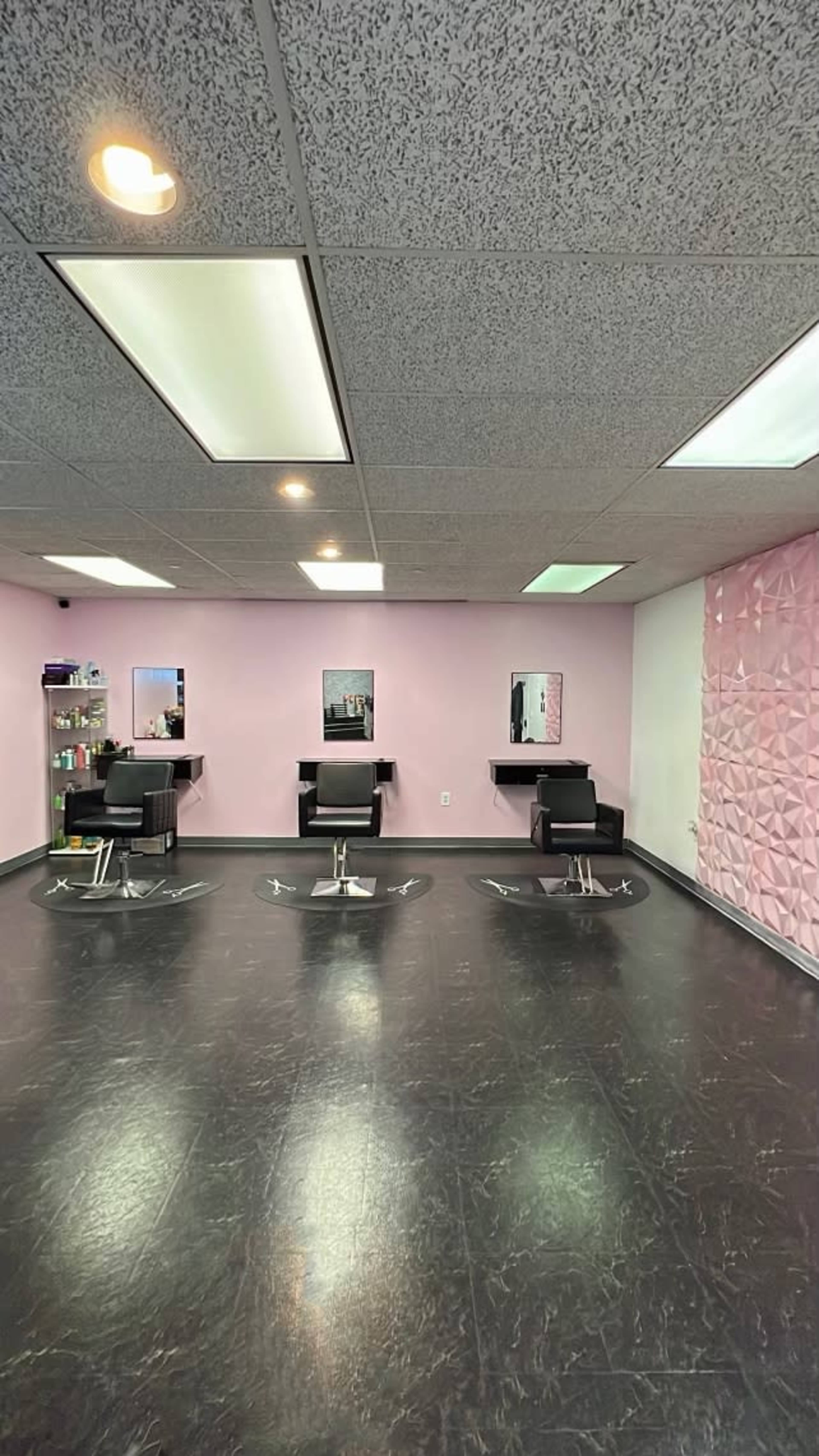 A hair salon interior with three styling chairs, mirrors, and a textured pink wall.