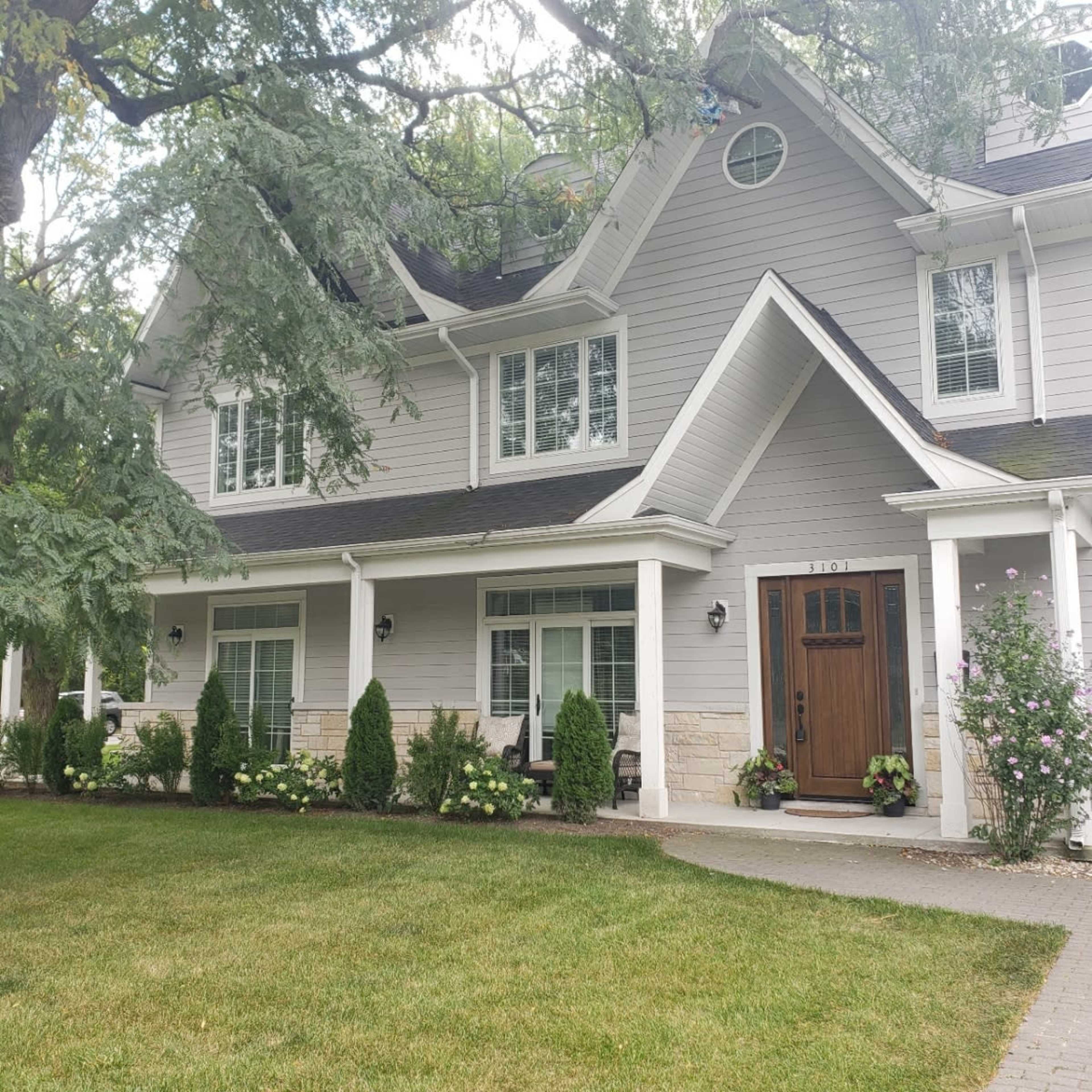 A two-story, gray-clapboard house with a stone-accented entrance and neatly landscaped surroundings.