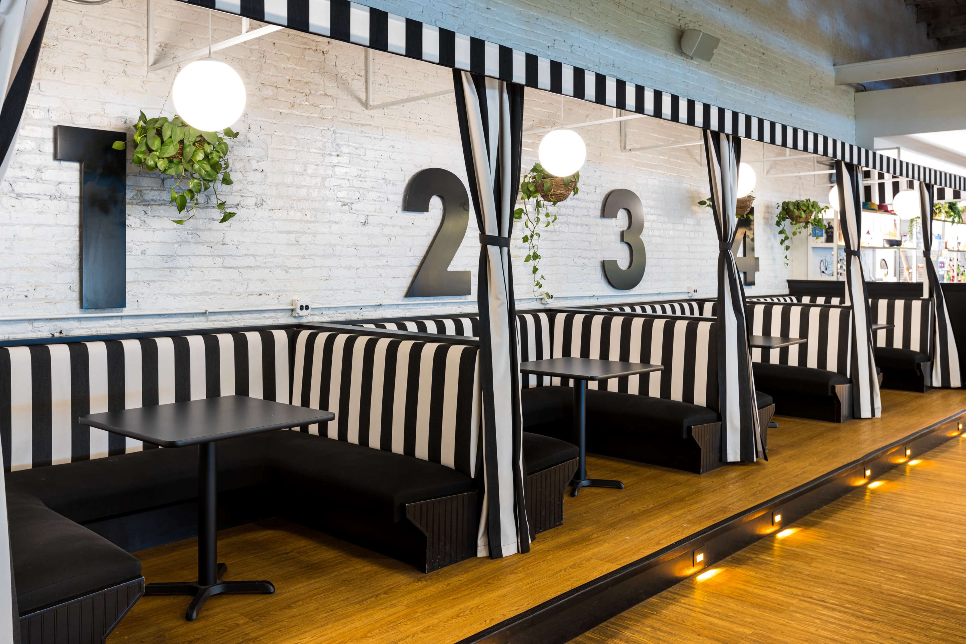 The image shows a modern cafe with black and white striped booth seating, separated by curtains and numbered 1 to 4 along a brick wall.