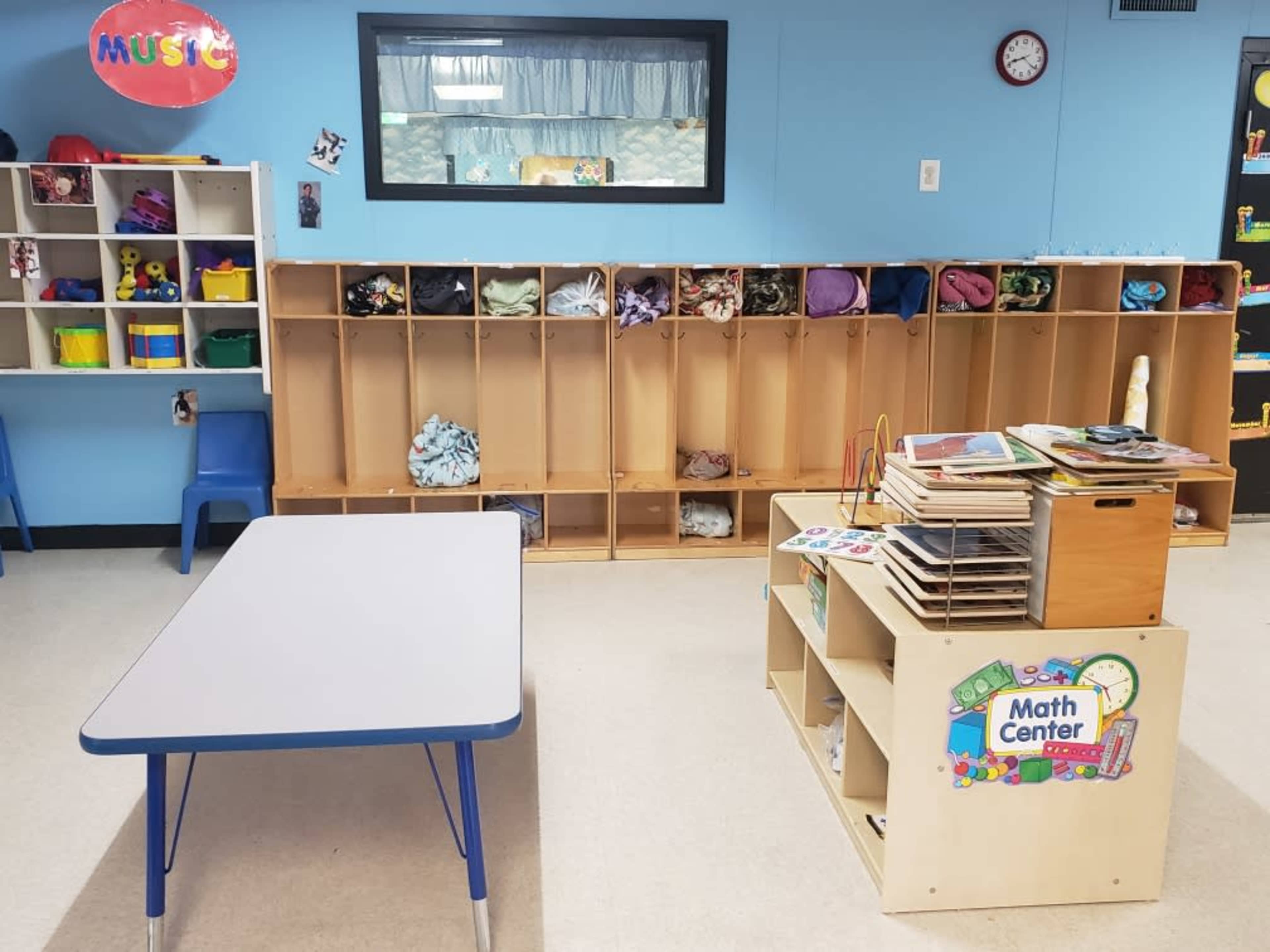 A classroom with cubby storage on one wall, a table in the center, and a play center labeled "Math Center."