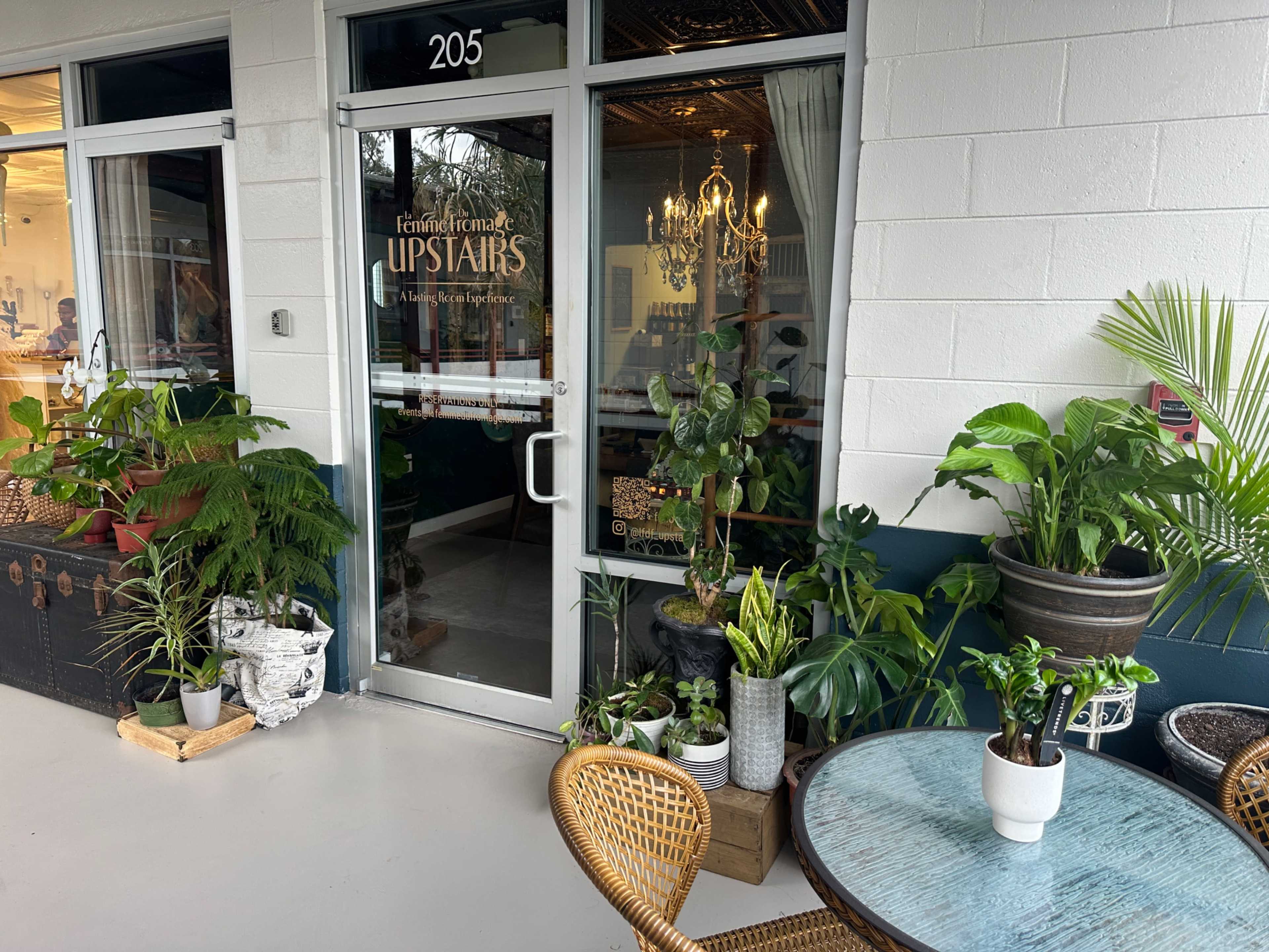 The image shows an entrance to a business labeled "UPSTAIRS" with large potted plants and a decorative table outside.