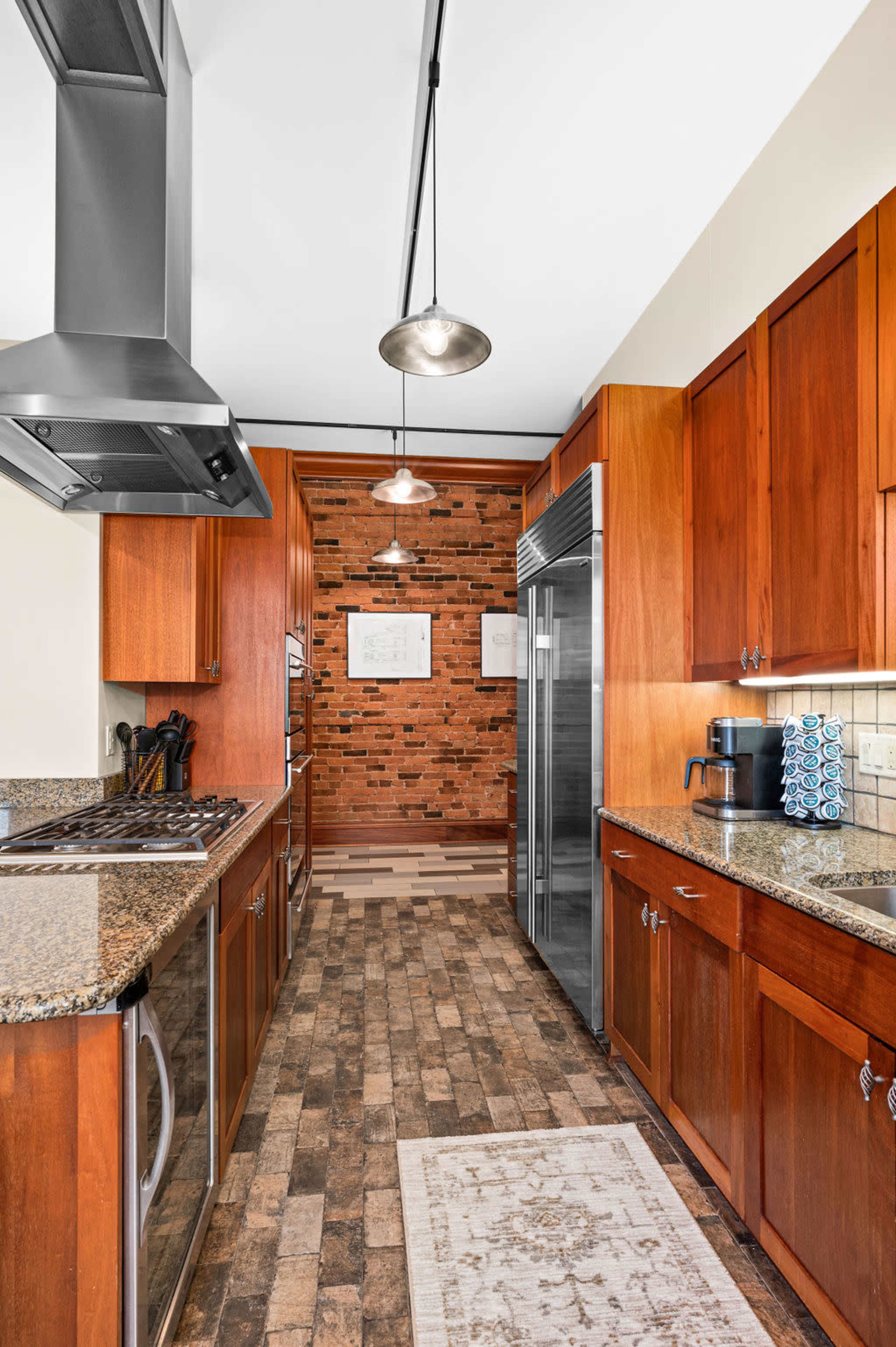 A modern kitchen features dark wooden cabinets, granite countertops, and a brick wall adorned with framed artwork.