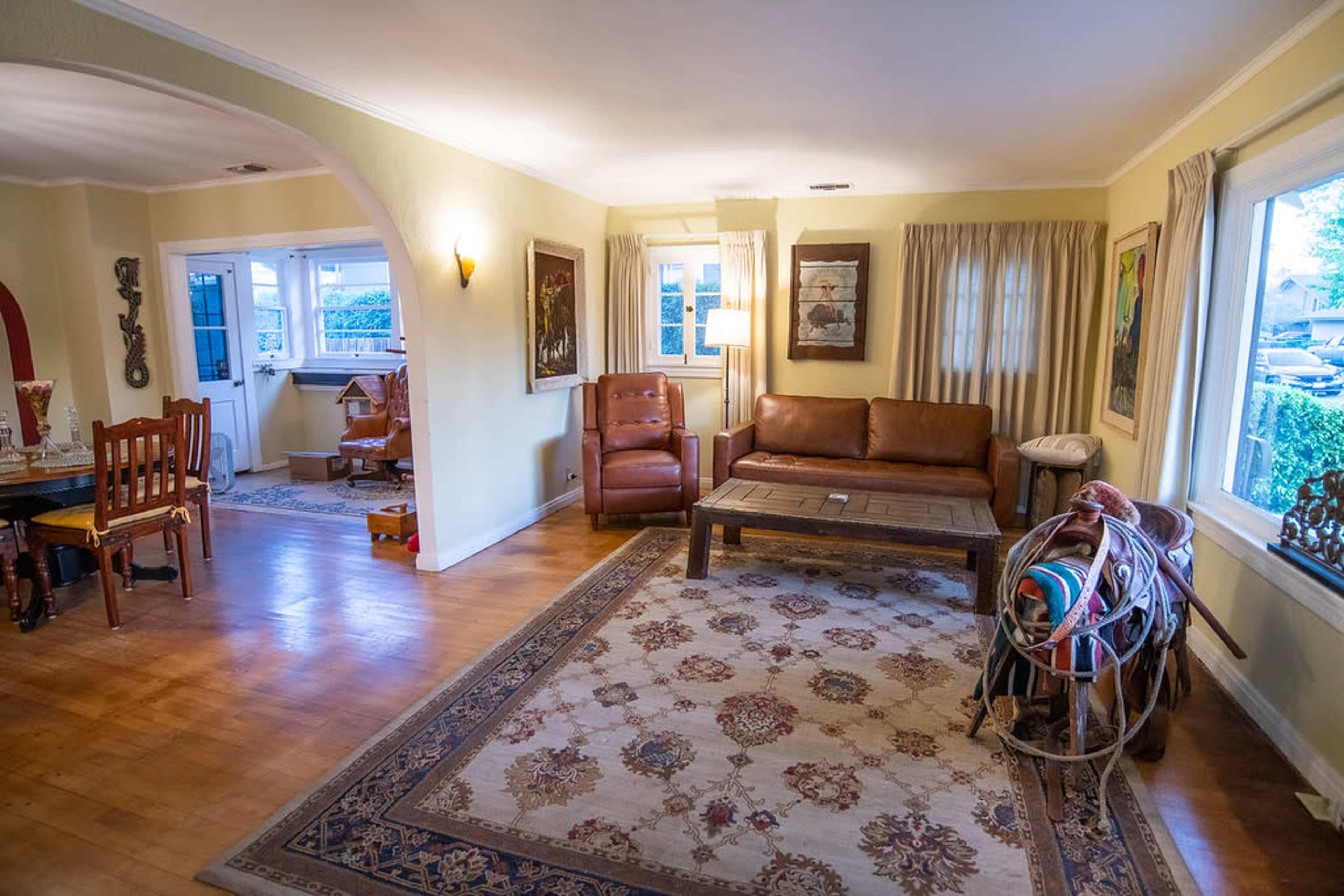 The image shows a cozy living space featuring a leather couch, a wooden coffee table, and a rug, with adjacent areas visible that include a dining area and a separate room.