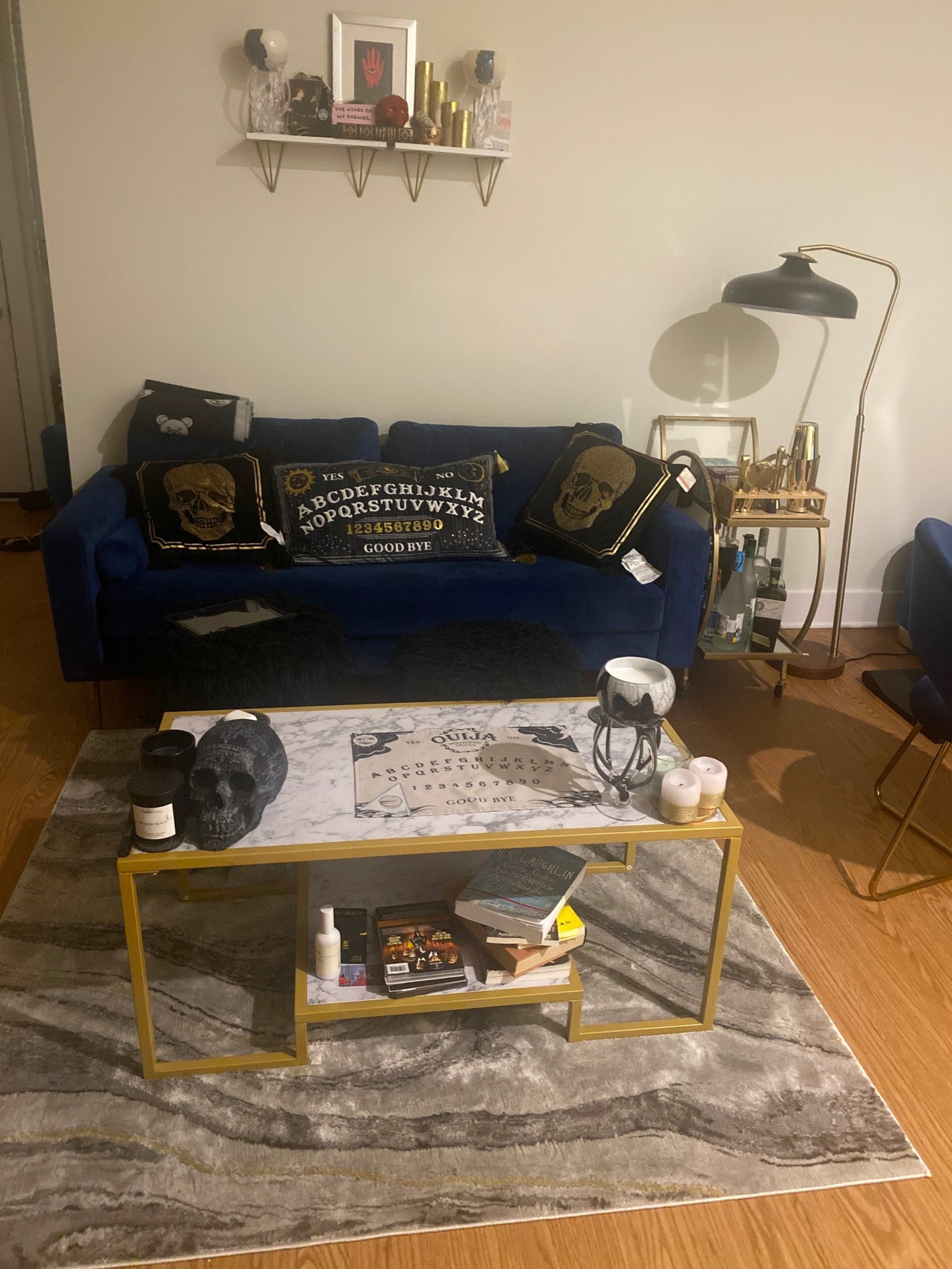 The living room features a blue sofa with decorative pillows, a marble coffee table with books and decor items, and a gold lamp beside it.