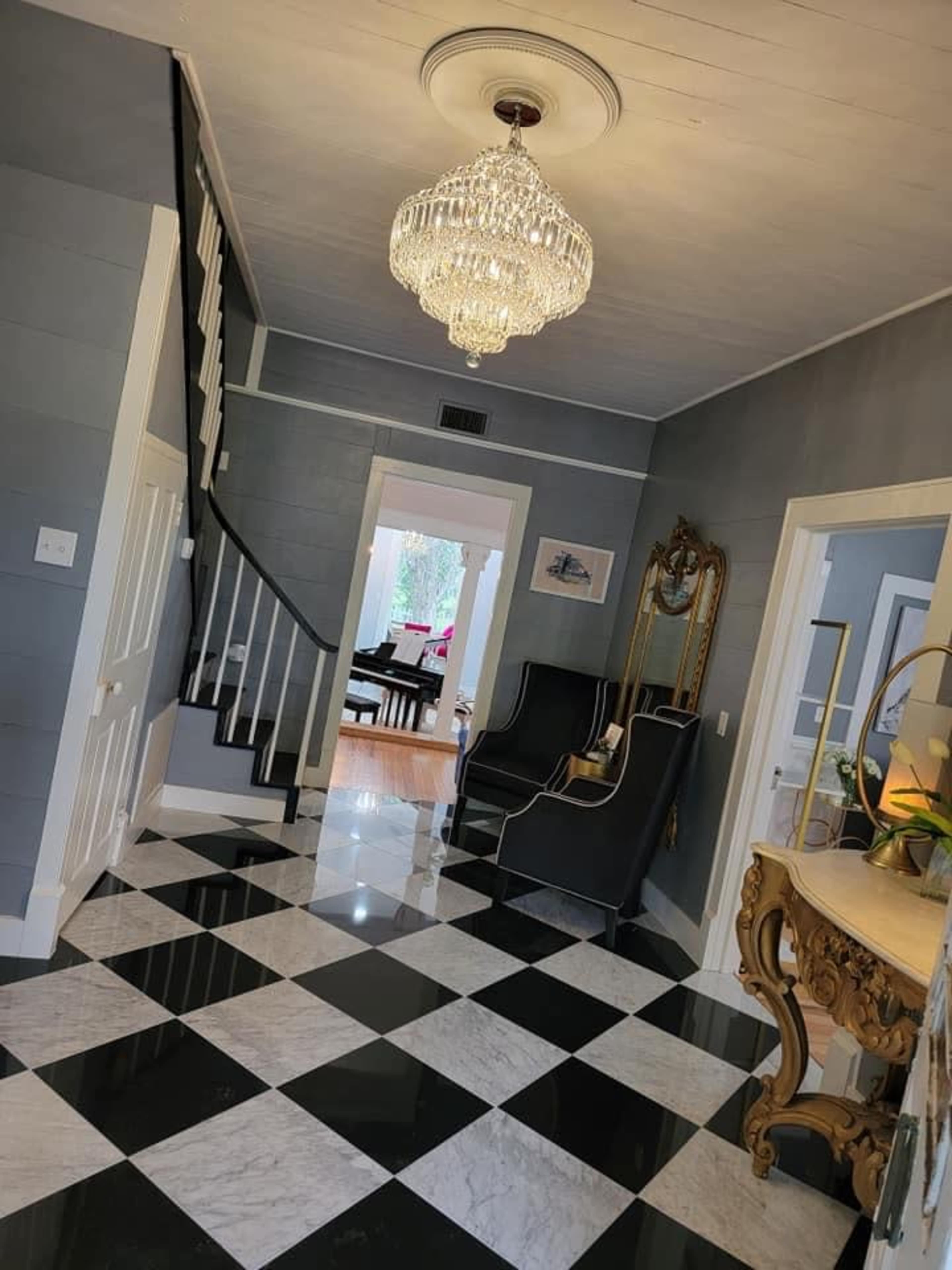 A hallway with a black and white checkered floor, a staircase with a black railing, a chandelier, and openings leading to other rooms.