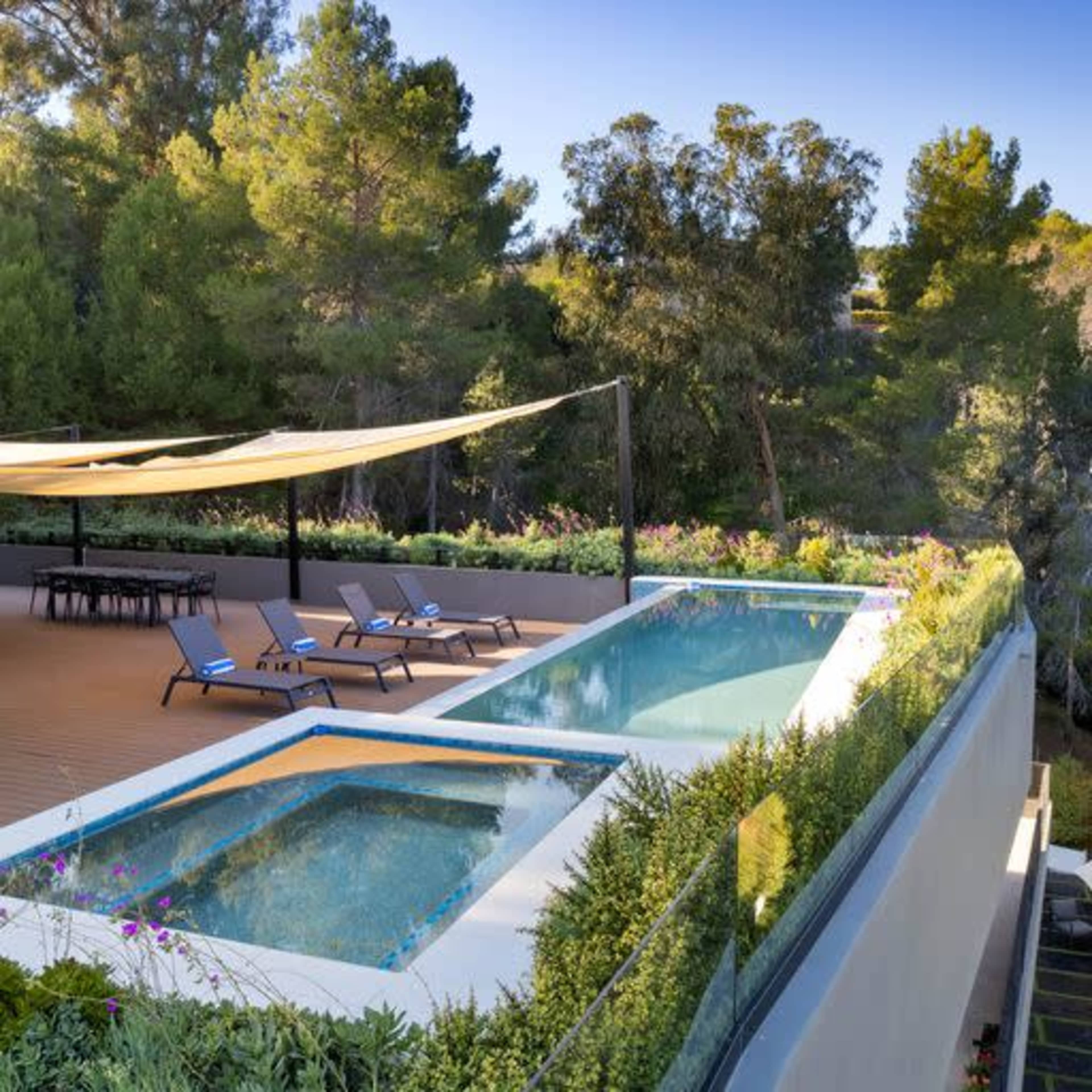 A serene outdoor area features a modern infinity pool bordered by greenery and lounge chairs under a shaded canopy.
