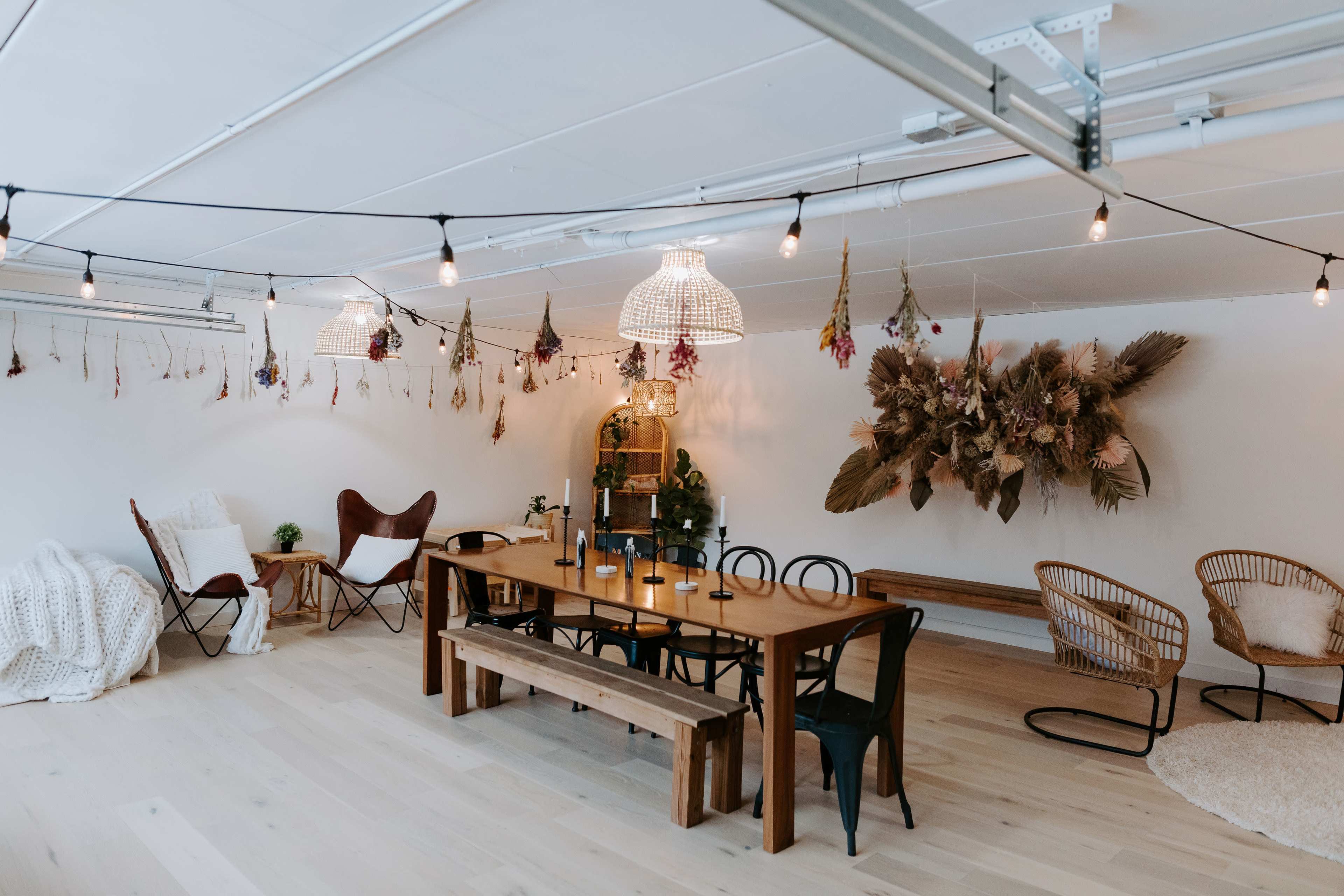 The image depicts a spacious room with a long wooden dining table surrounded by various seating arrangements and decorative wall hangings.