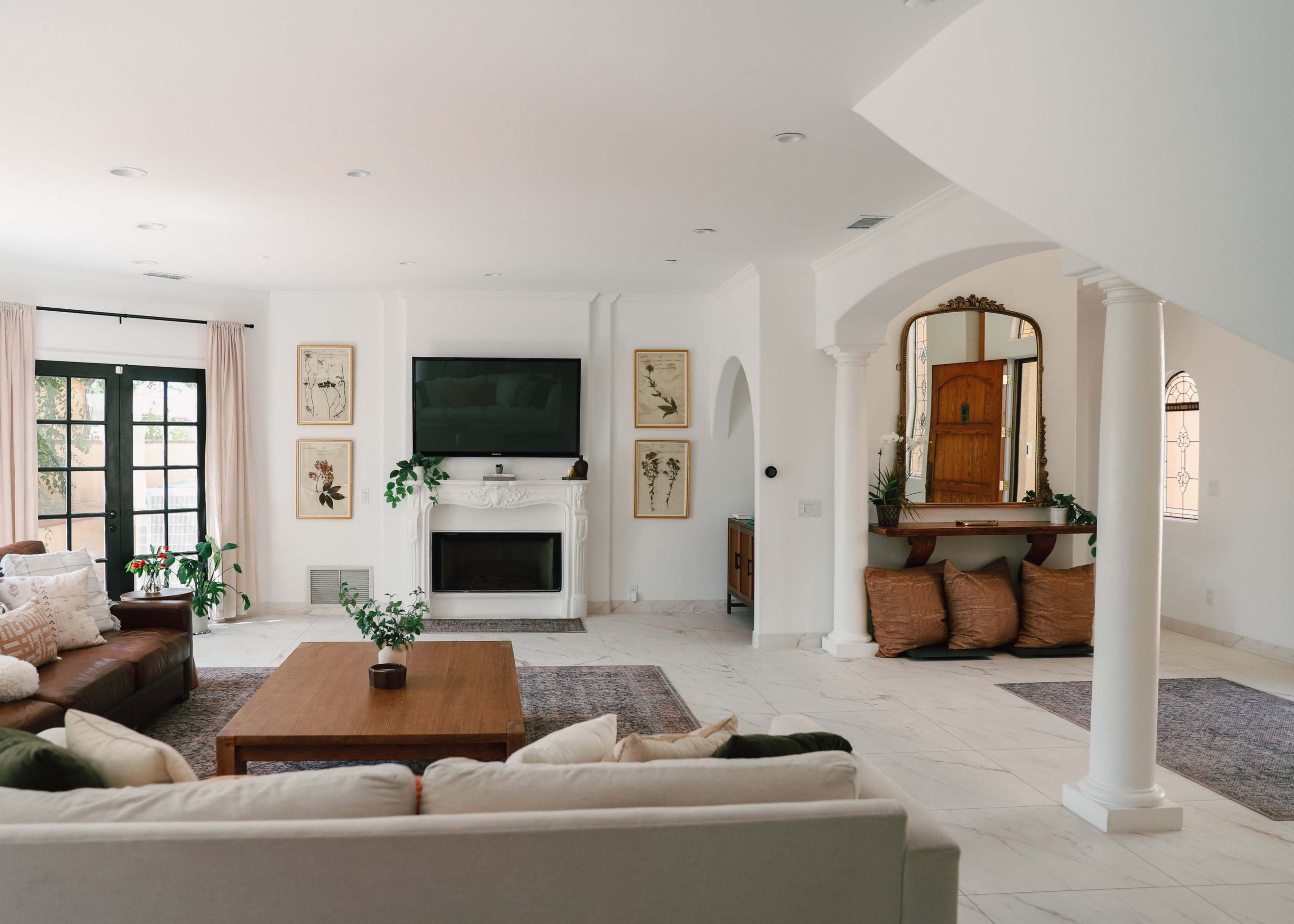 The image shows a spacious living room featuring a fireplace, a large television, and a wooden coffee table surrounded by seating areas.