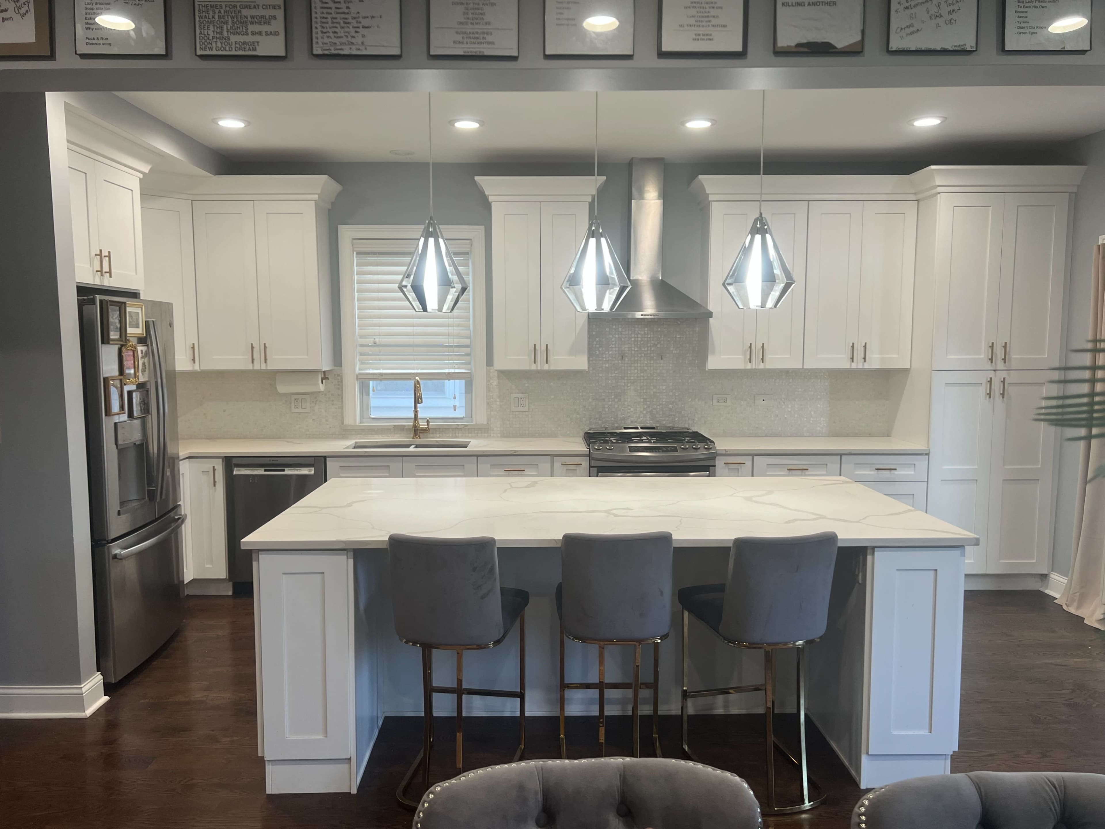 The image shows a modern kitchen with white cabinetry, a large island with seating, stainless steel appliances, and pendant lighting.