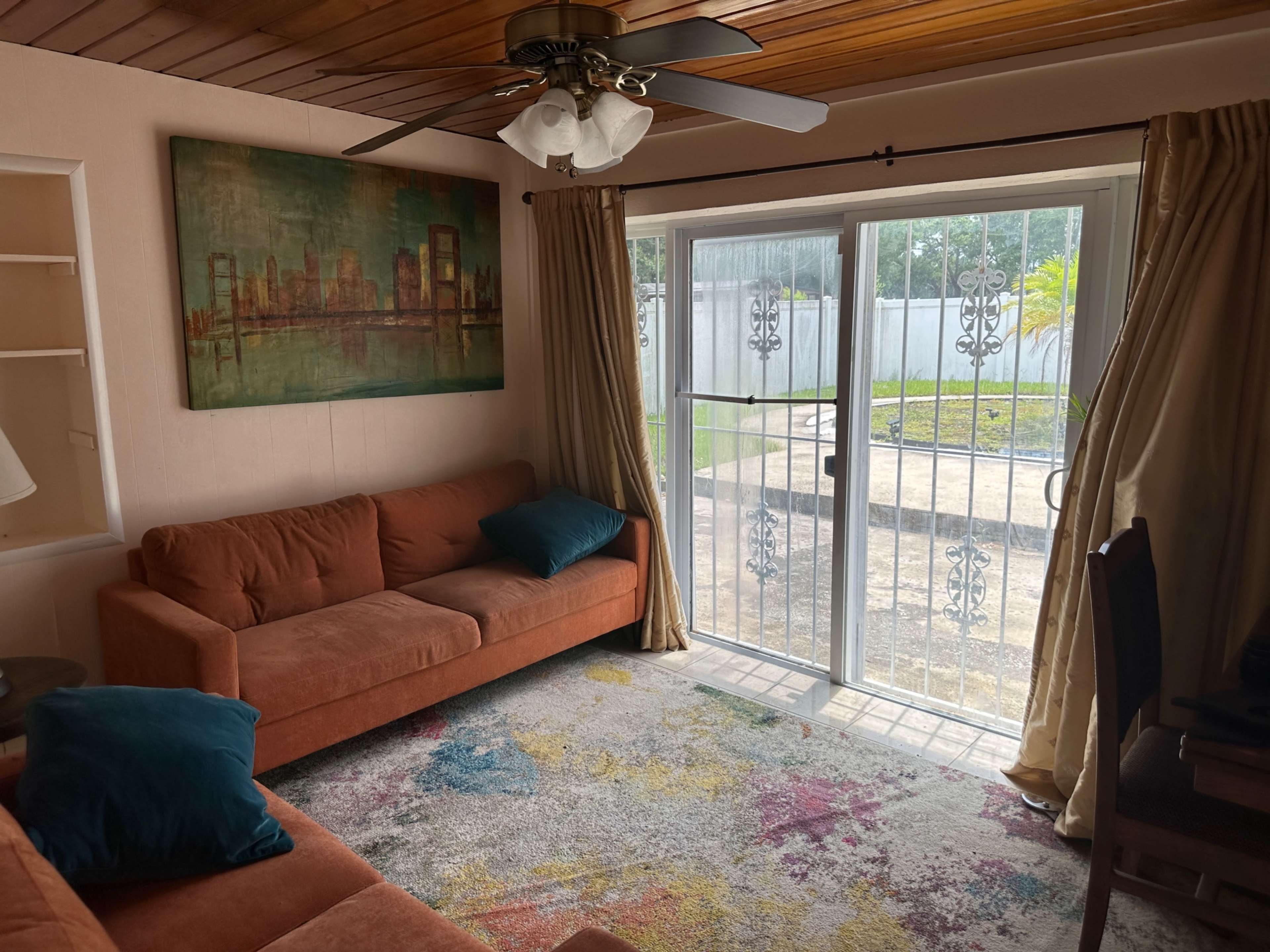 A living room with an orange sofa, a colorful rug, and sliding glass doors leading to a patio.