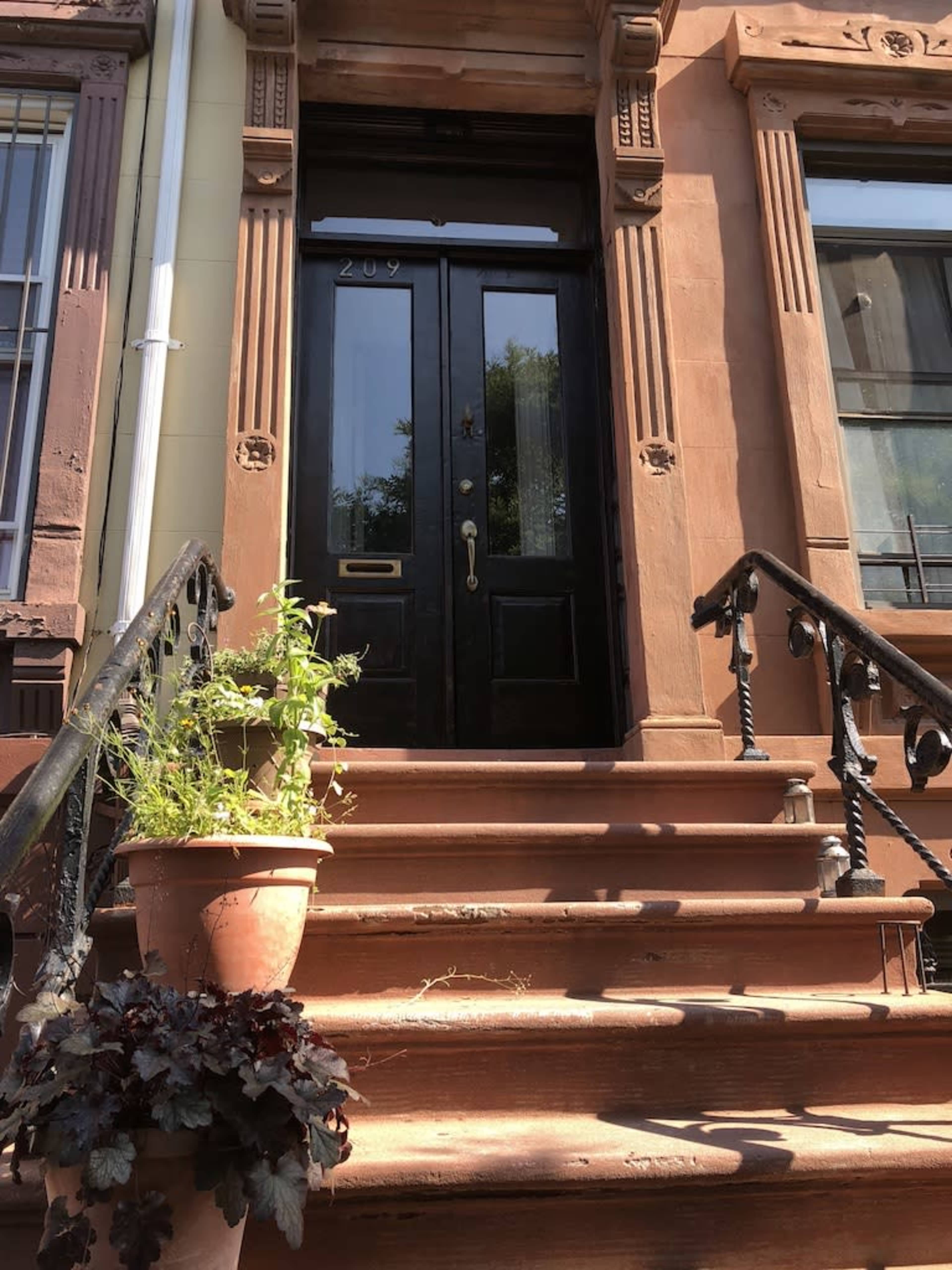 A set of stairs leading up to a black front door, framed by decorative stonework and flanked by potted plants.