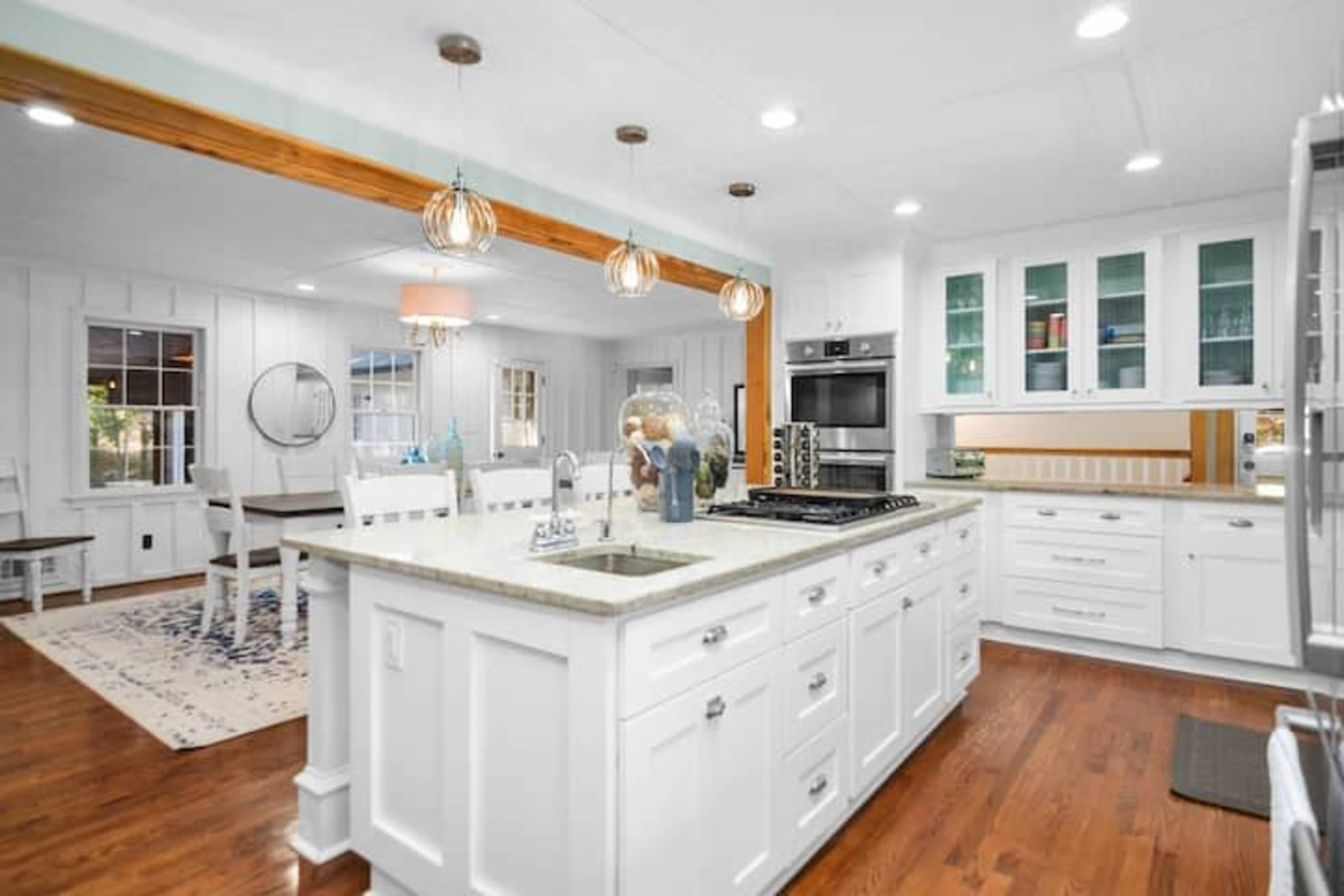 A modern kitchen with white cabinets, a central island with a gray countertop, and stainless steel appliances, opening into a dining area with a round table and chairs.