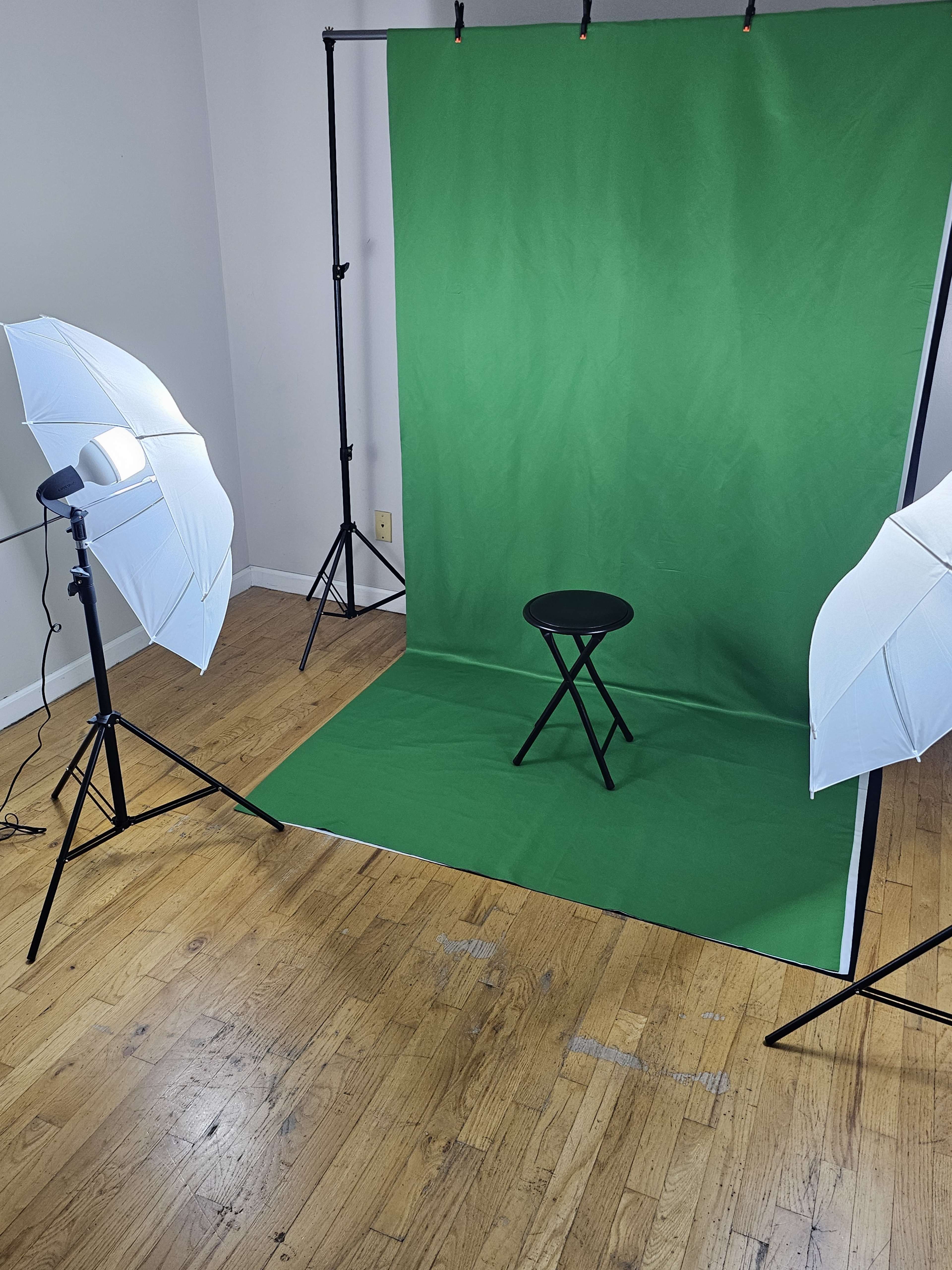 The image features a photography setup with a green backdrop, a black stool in the center, and two softbox lights positioned on either side.