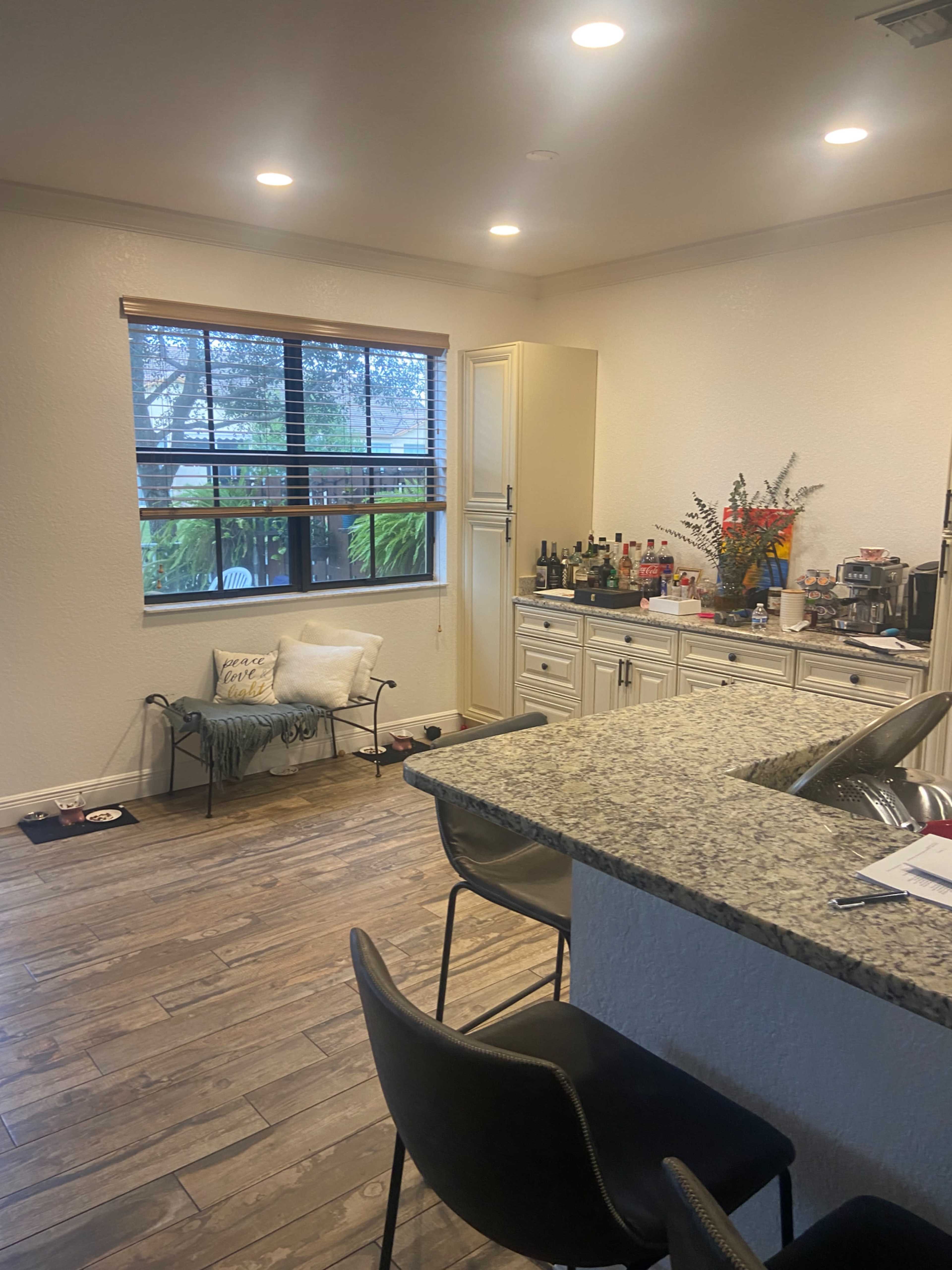A modern kitchen features a granite countertop, a bar area with two chairs, and a window that provides natural light while showcasing some greenery outside.