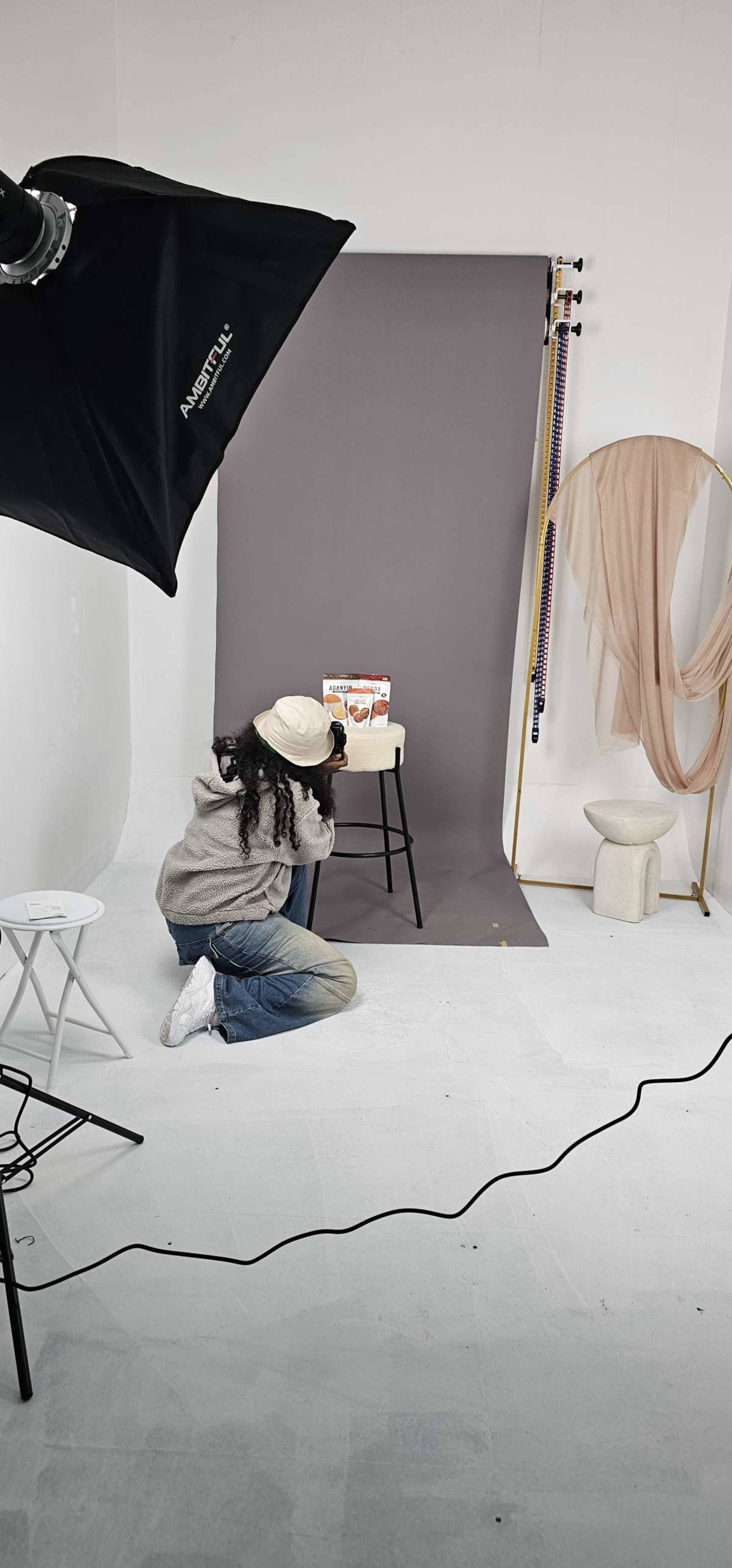 A person is kneeling and photographing a small display on a stool against a gray background in a studio setting.