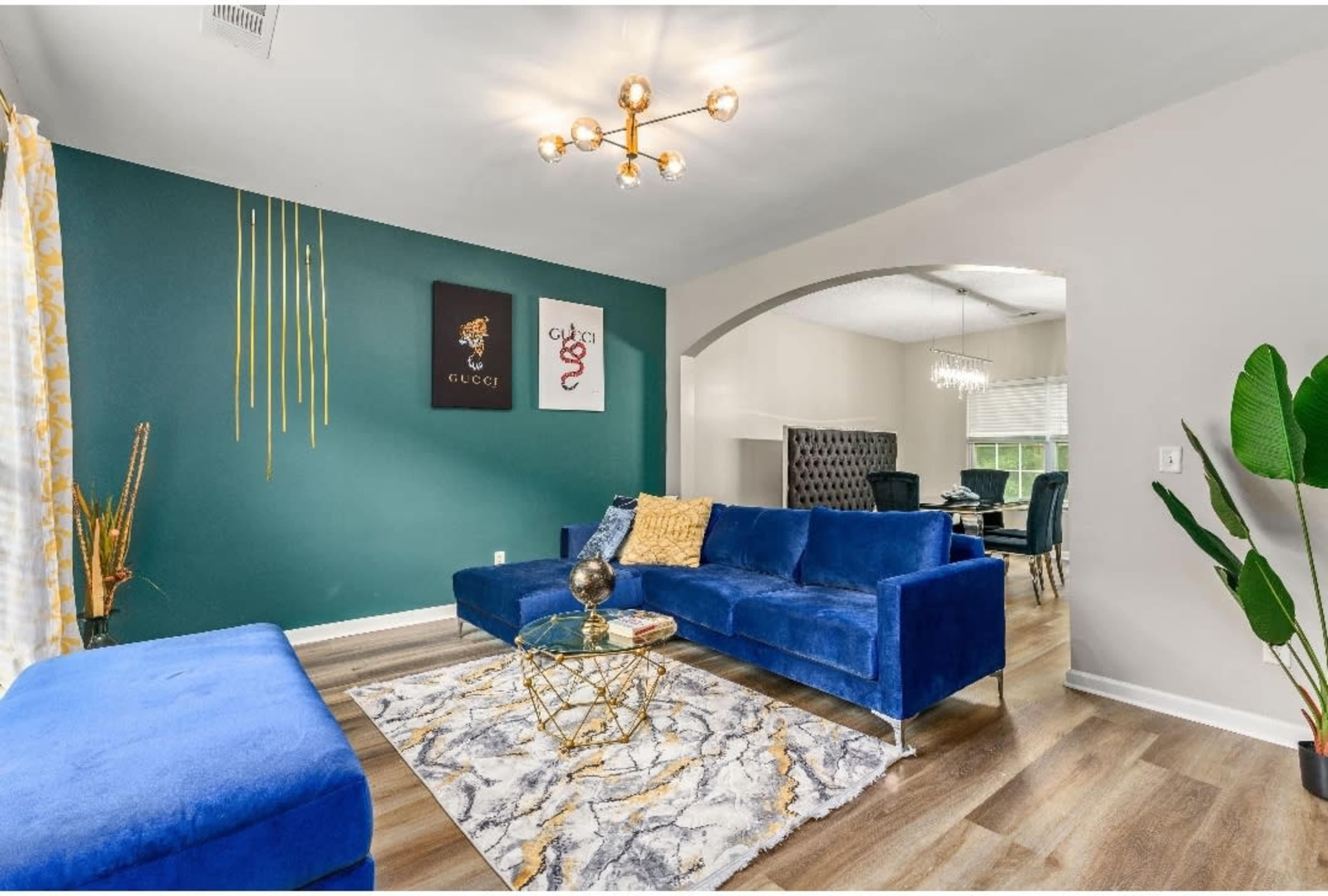 A modern living room featuring a blue velvet sofa, a geometric coffee table, and a decorative rug, with green and yellow accent walls.
