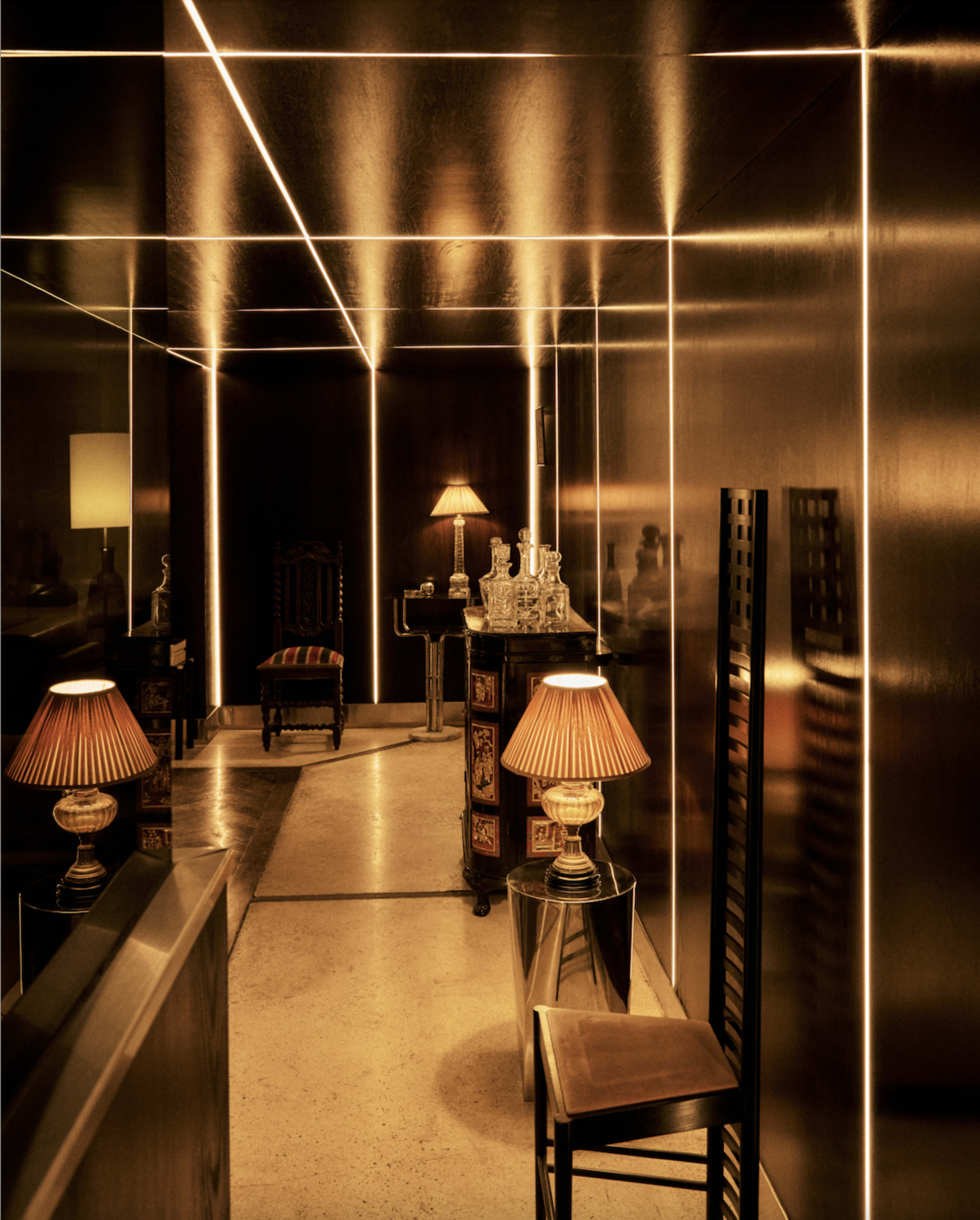 A dimly lit corridor features sleek metallic walls, illuminated by linear lighting, with vintage lamps and ornate furniture creating an elegant atmosphere.