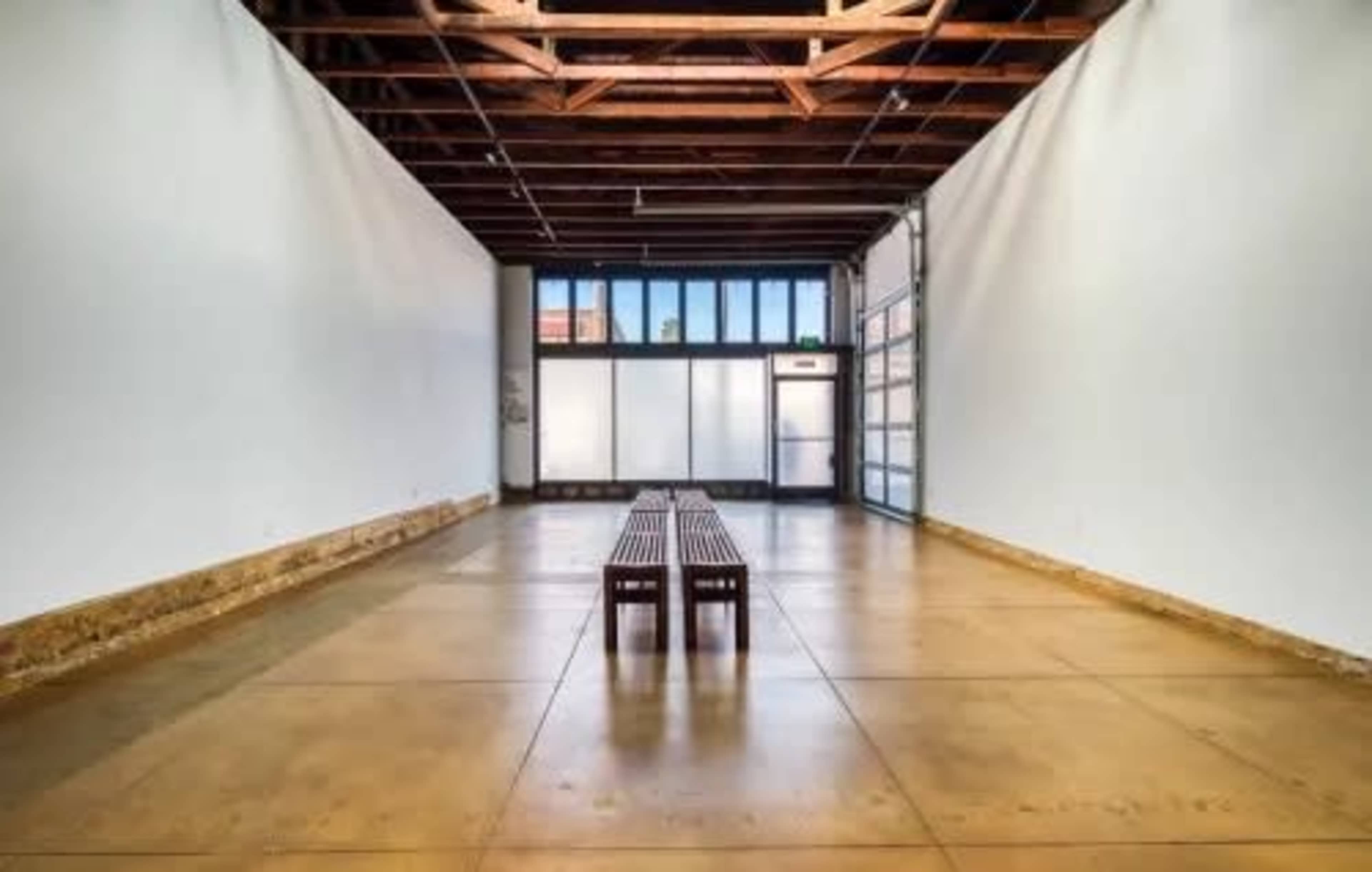 A spacious interior with a wooden bench centered on a polished concrete floor, flanked by white walls and large windows at the front.
