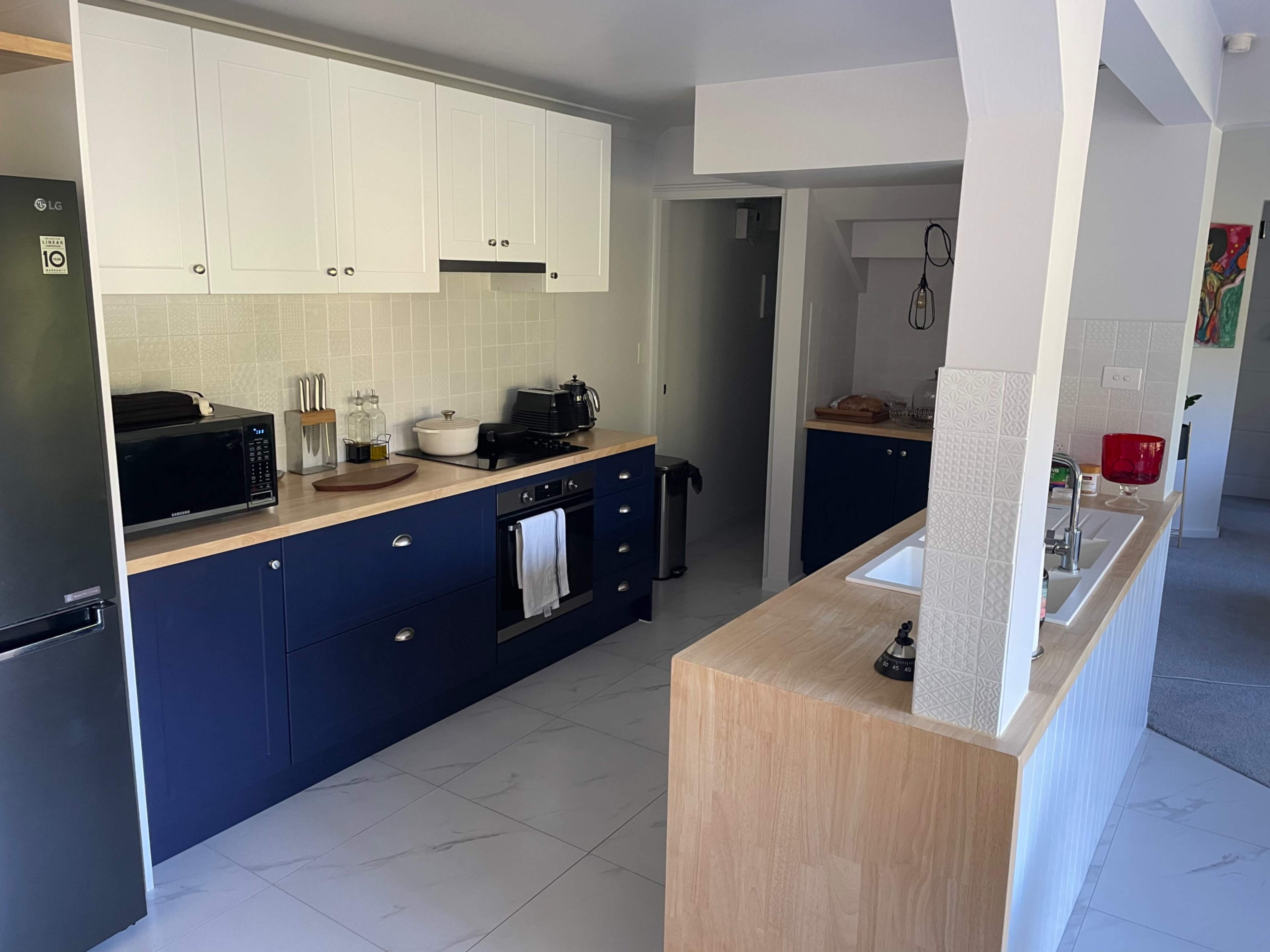 A modern kitchen with navy blue cabinetry, wooden countertops, and white tile accents.